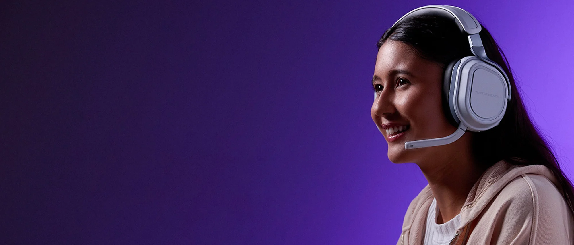 Une femme souriante portant un casque de jeu blanc sur fond violet.