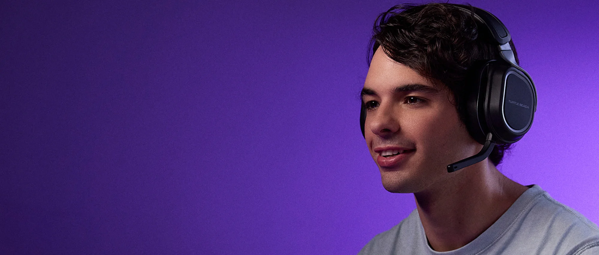 Un jeune homme portant un casque avec microphone sourit sur un fond violet.