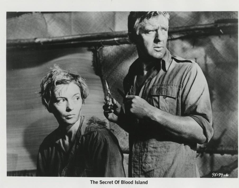 Ein Mann hält eine Schere und schneidet einer Frau im Film 'The Secret Of Blood Island' die Haare.