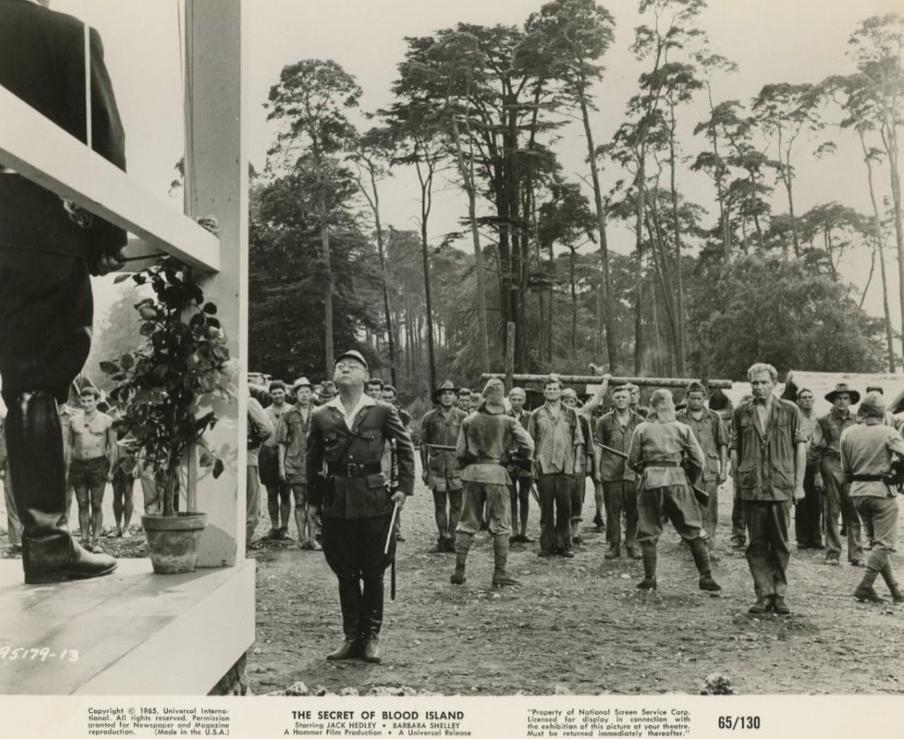 Schwarzweißfoto zeigt einen japanischen Offizier, der vor gefangenen Soldaten im Dschungel steht.