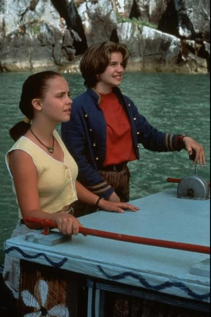 Zwei junge Mädchen stehen auf einem fahrenden Boot vor einer felsigen Küste.
