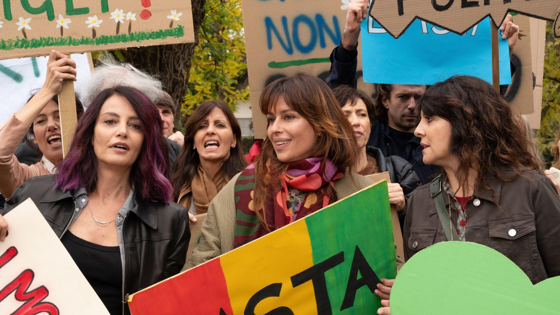 Menschen versammeln sich zu einem Protest im Freien und halten bunte Schilder mit Botschaften hoch.