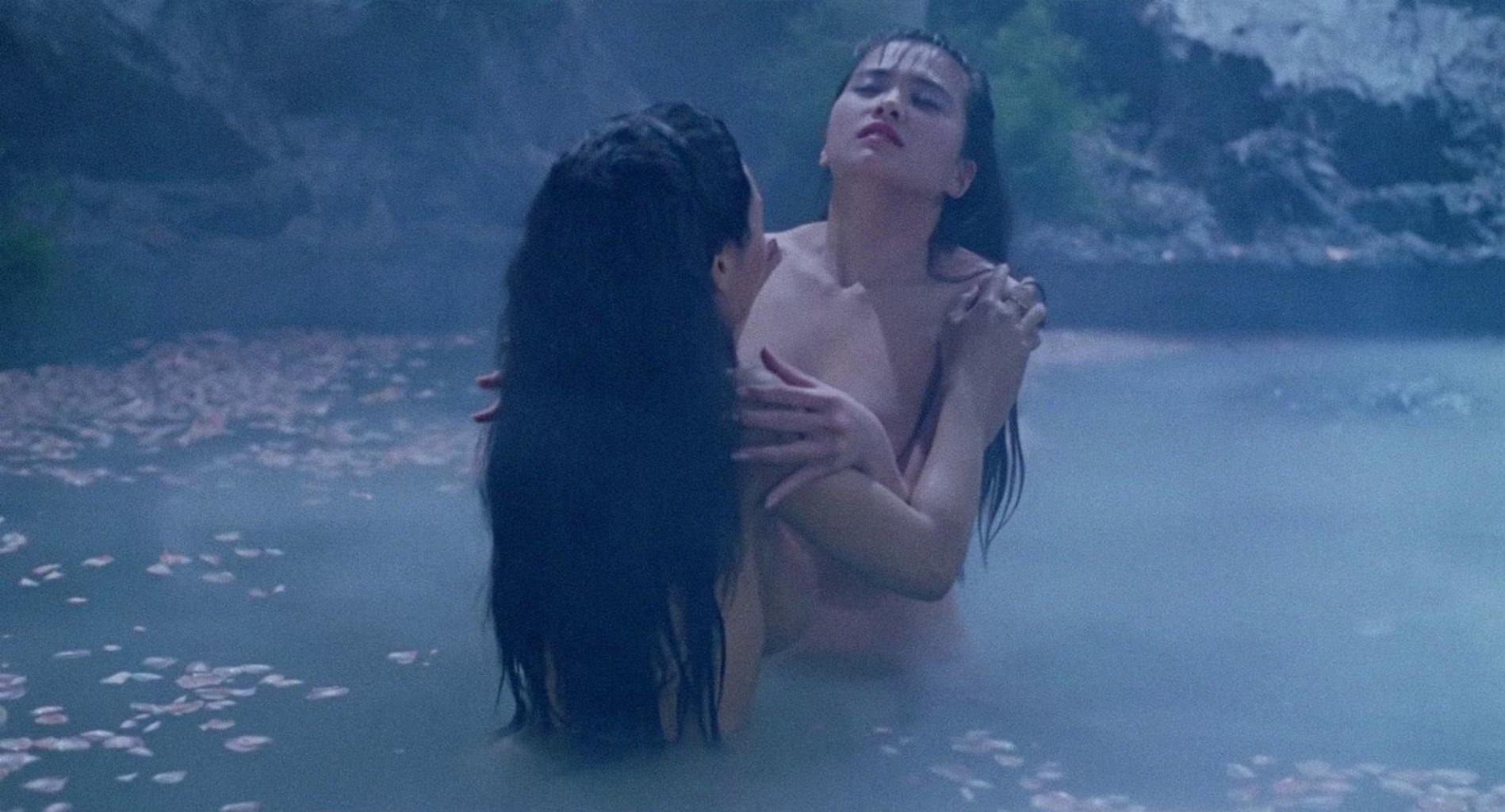 Zwei Frauen mit langem dunklem Haar umarmen sich in einem nebligen Pool voller Blütenblätter.