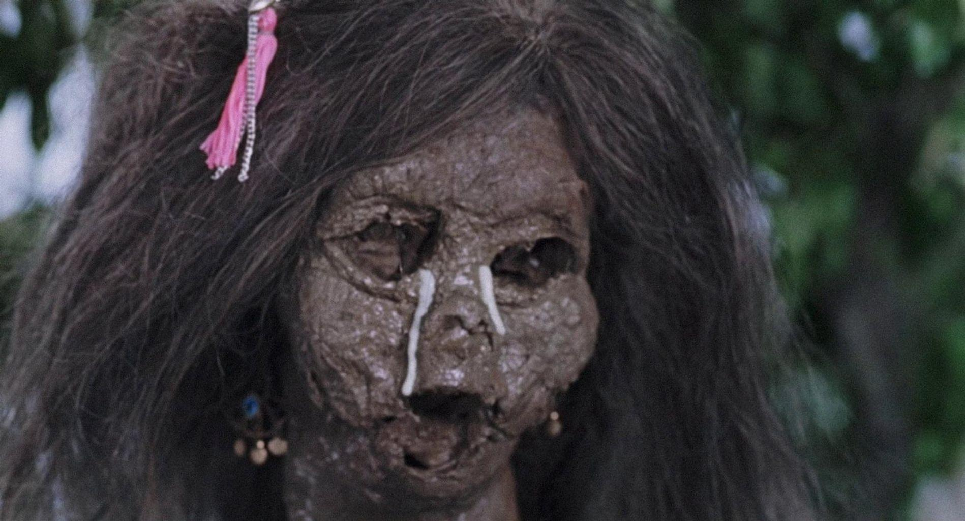 Eine schlammbedeckte Puppe mit langem dunklen Haar und einer pinken Schleife hat weiße Flüssigkeit, die aus ihren Augen läuft.