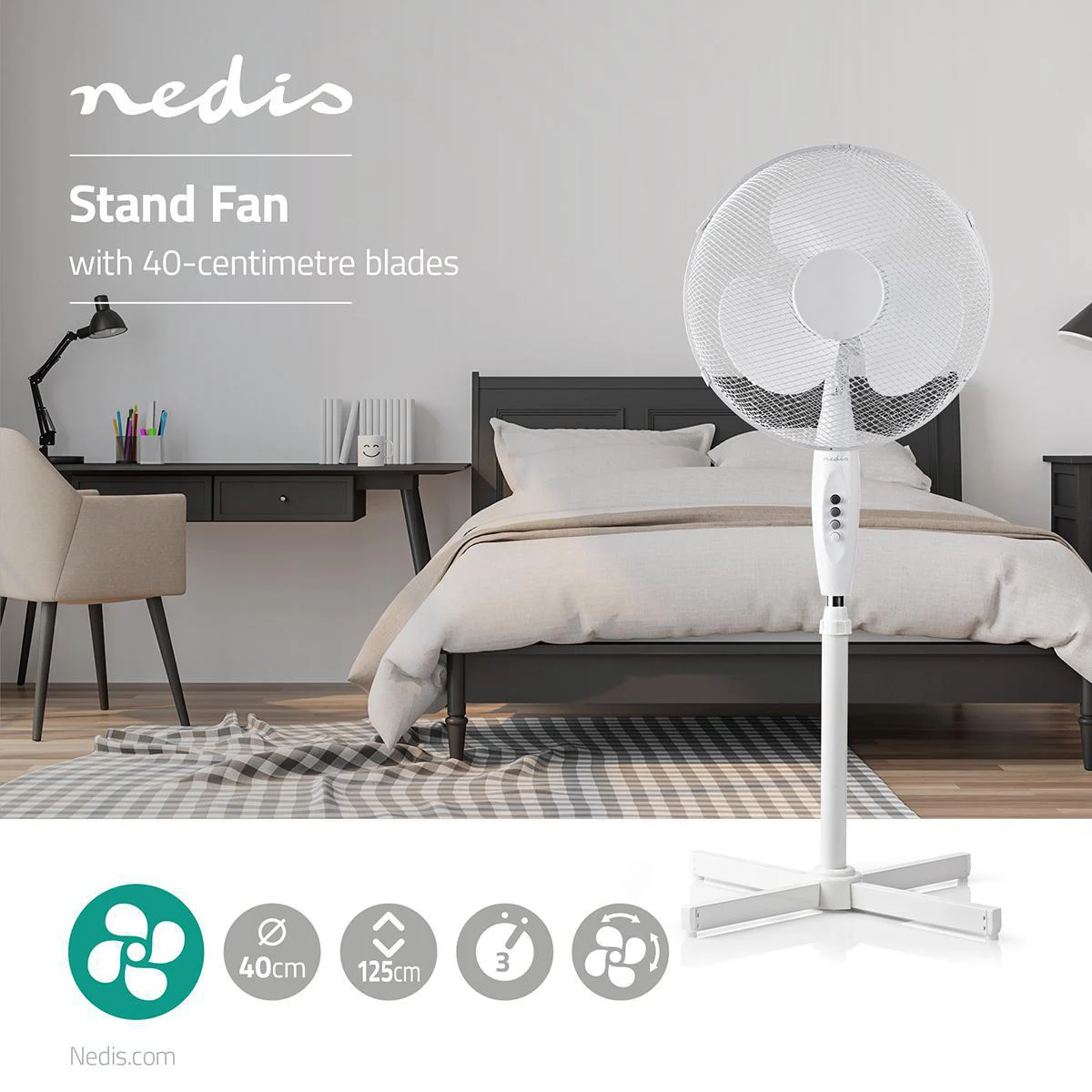 Ein weißer Standventilator steht in einem Schlafzimmer, mit Bett und Schreibtisch im Hintergrund.