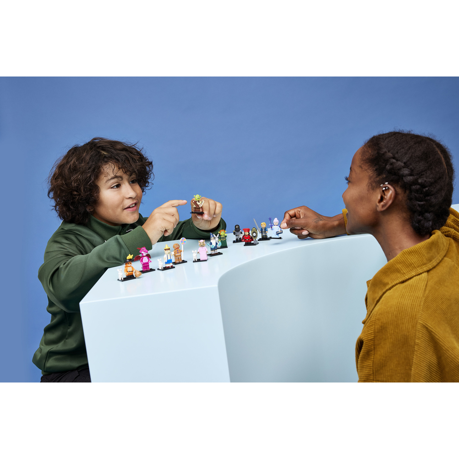Due bambini giocano con le minifigure Lego su un tavolo bianco con sfondo blu.