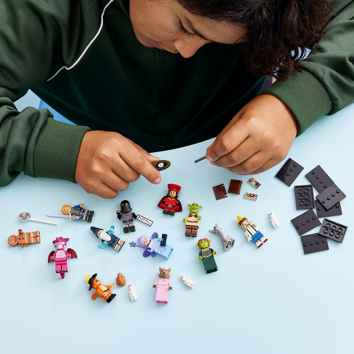 Un bambino costruisce con personaggi e mattoncini Lego su un tavolo azzurro.