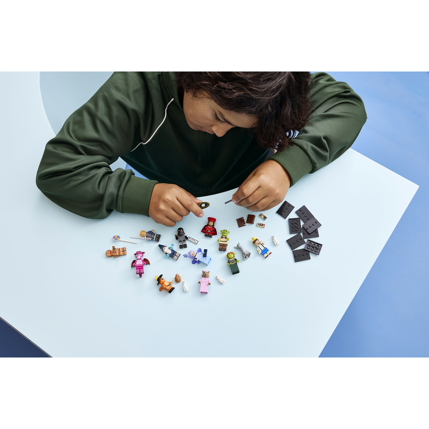 Un bambino con un maglione verde assembla minifigure LEGO su un tavolo.