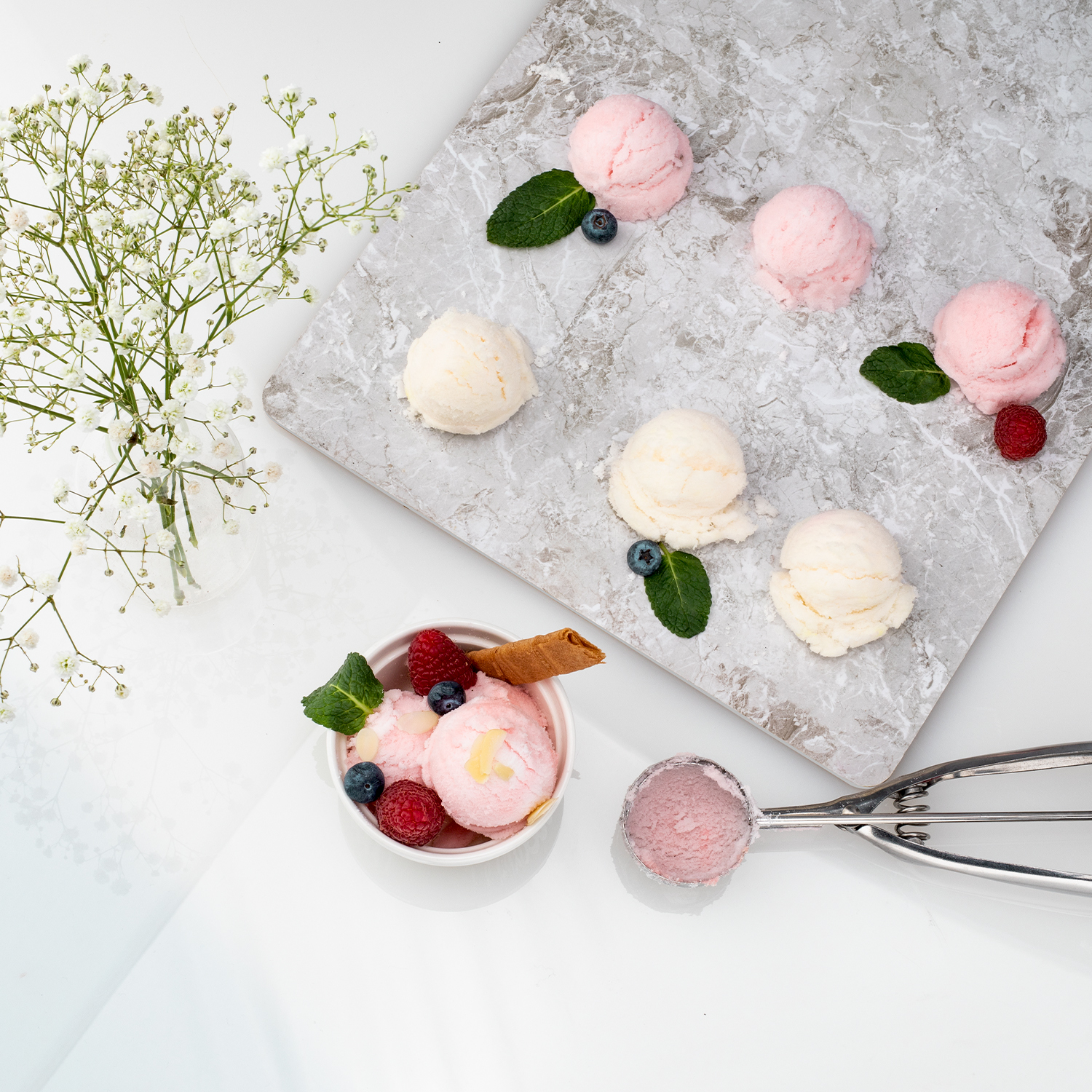 Palline di gelato rosa e bianche su marmo, con bacche, menta e fiori.