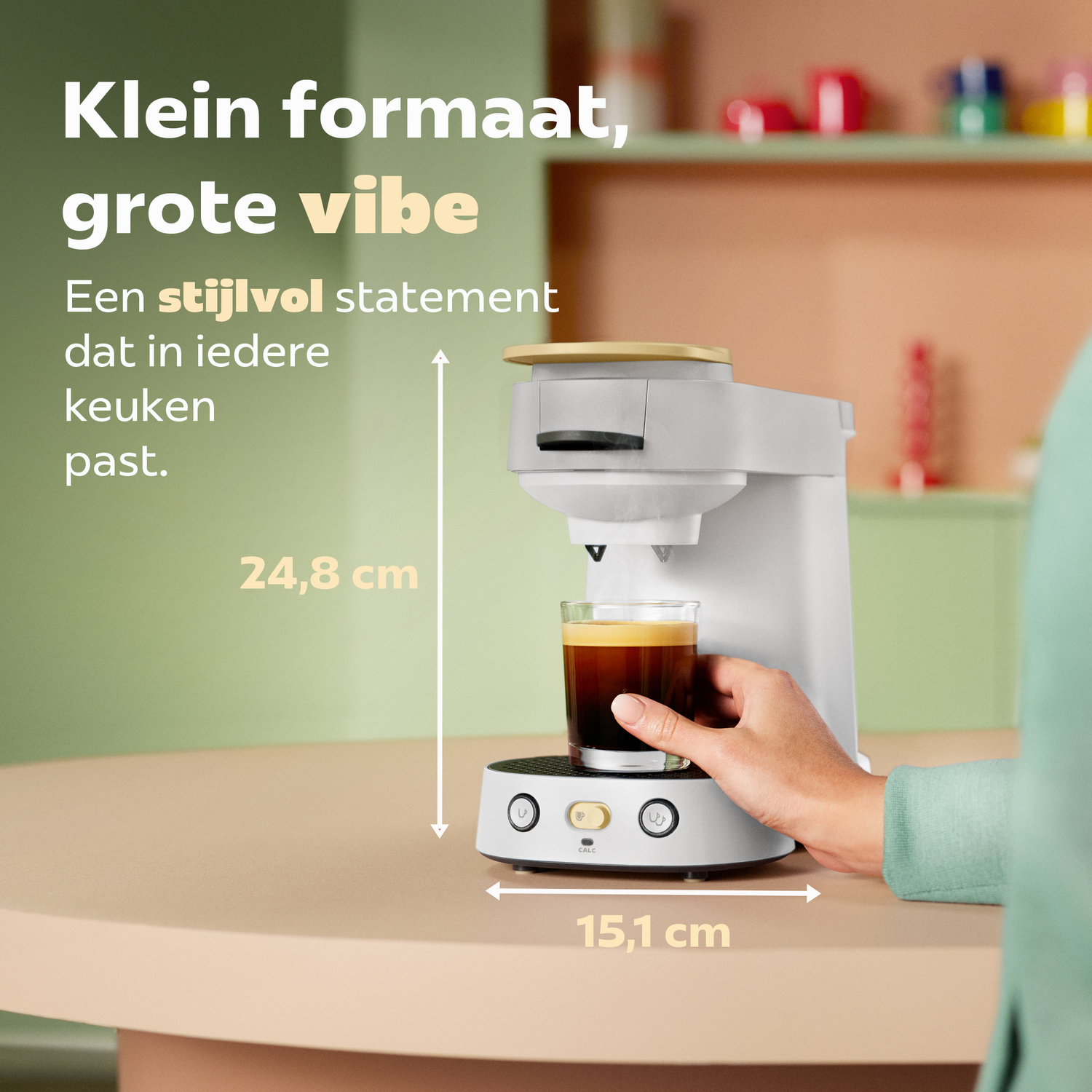 Compacte witte koffiemachine met glas op beige tafel en tekst.