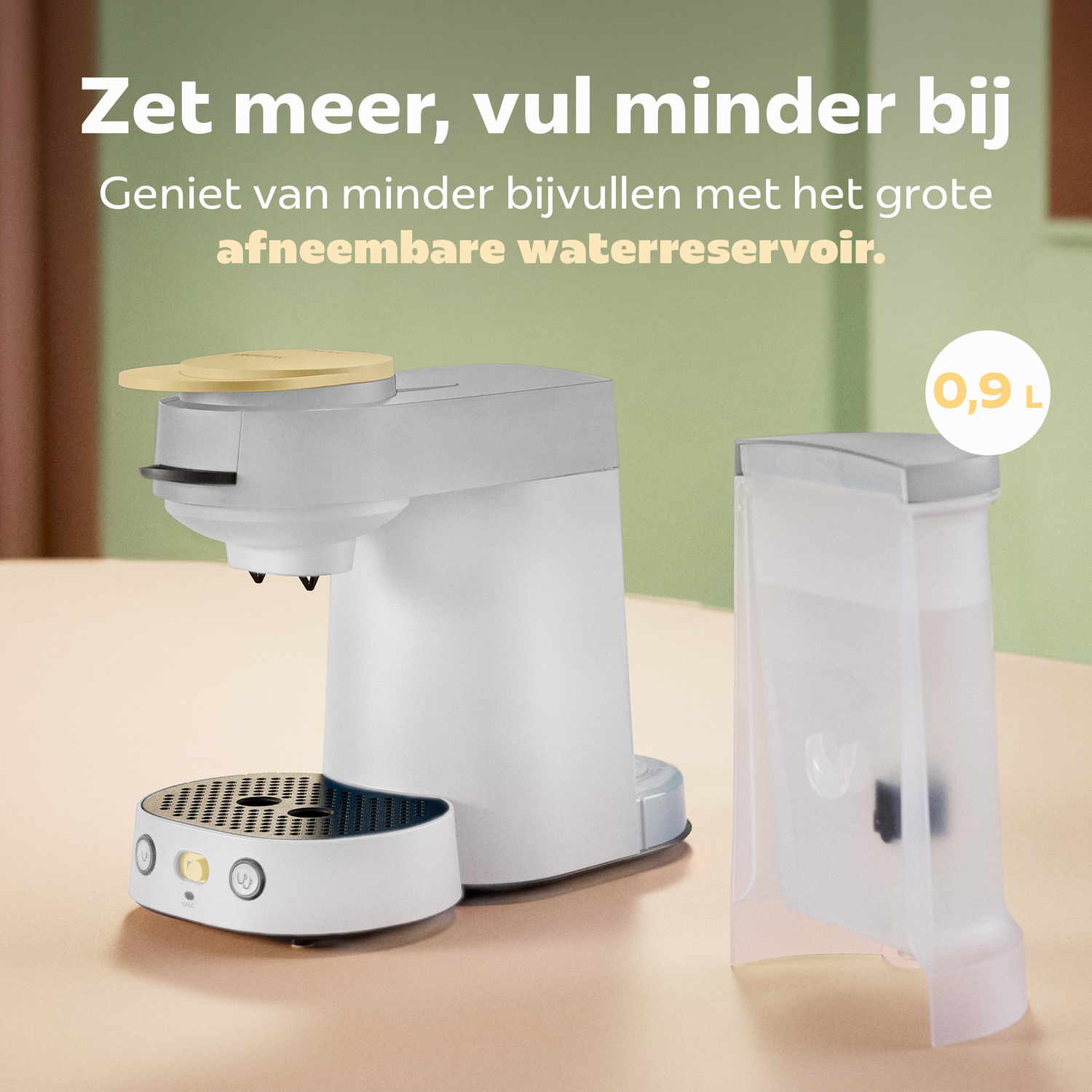 Een wit-grijze koffiemachine met een los waterreservoir van 0,9L op een houten oppervlak voor een groene muur.