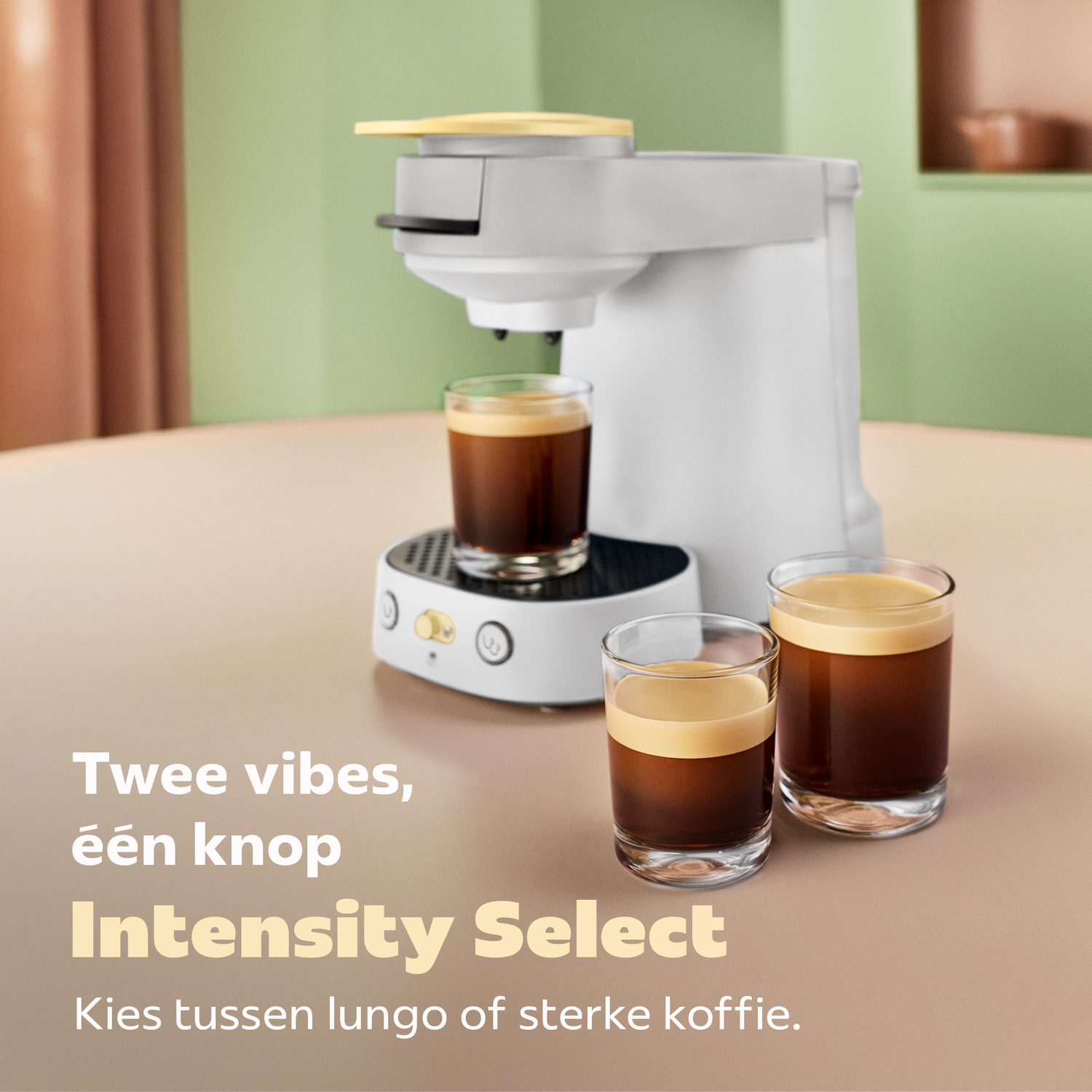 Een witte koffiemachine staat op een tafel met drie glazen koffie, tegen een groen en bruine achtergrond.