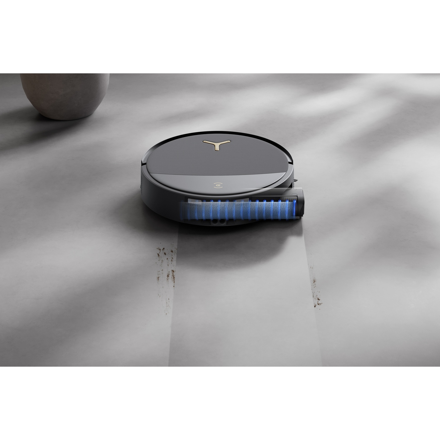 Un robot aspirapolvere nero pulisce un pavimento grigio, lasciando una scia pulita.
