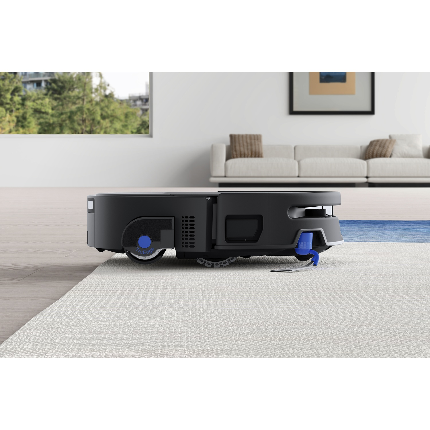 Un robot aspirapolvere nero su un tappeto chiaro in un soggiorno moderno con divano e finestra.