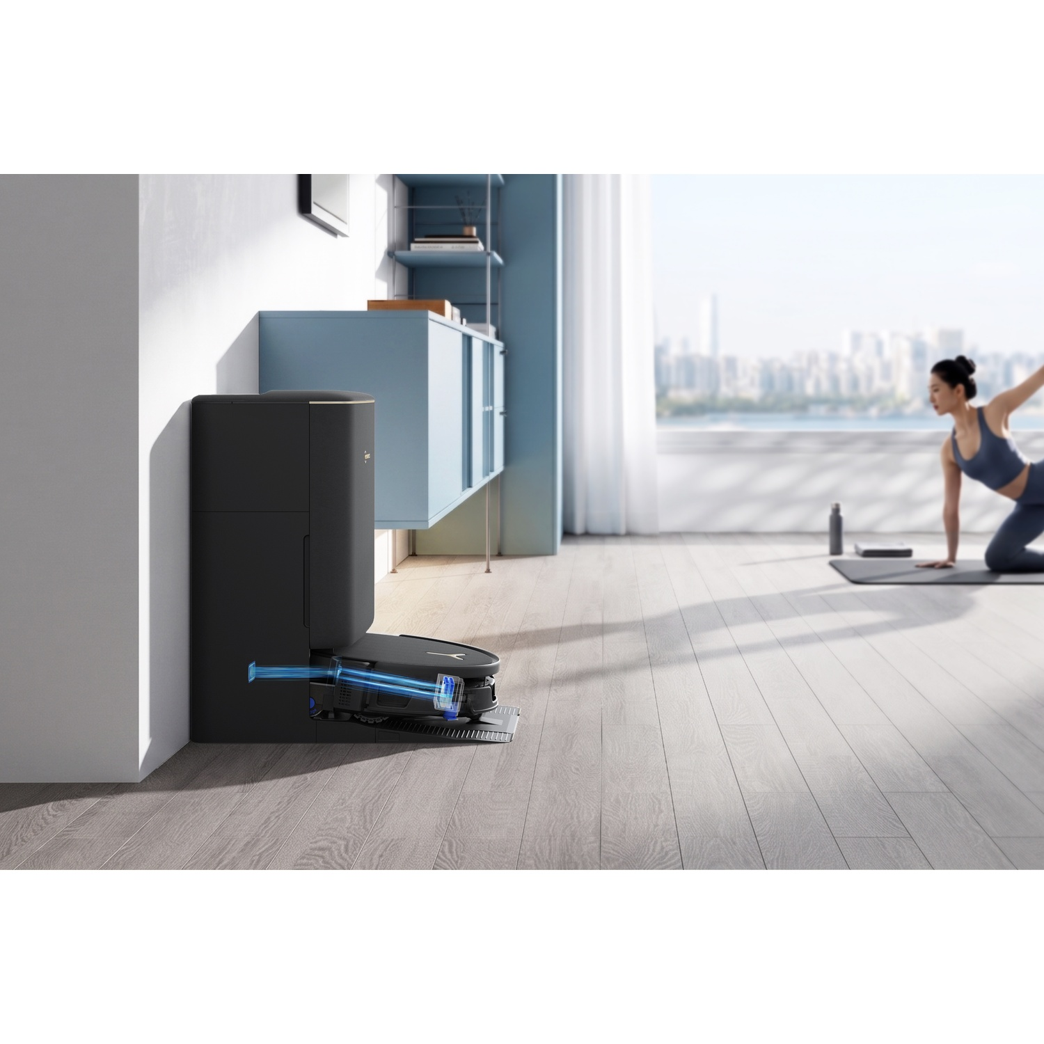 Un robot aspirapolvere nero sulla base su pavimenti in legno, con una donna che fa yoga.