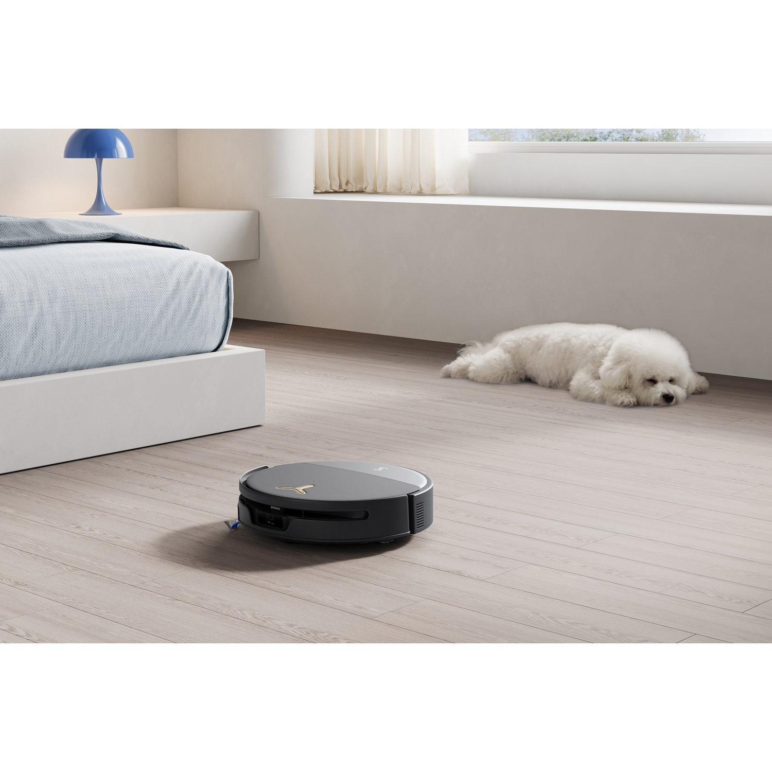 Un robot aspirapolvere su un pavimento in legno in una camera da letto, con un cane bianco che dorme.