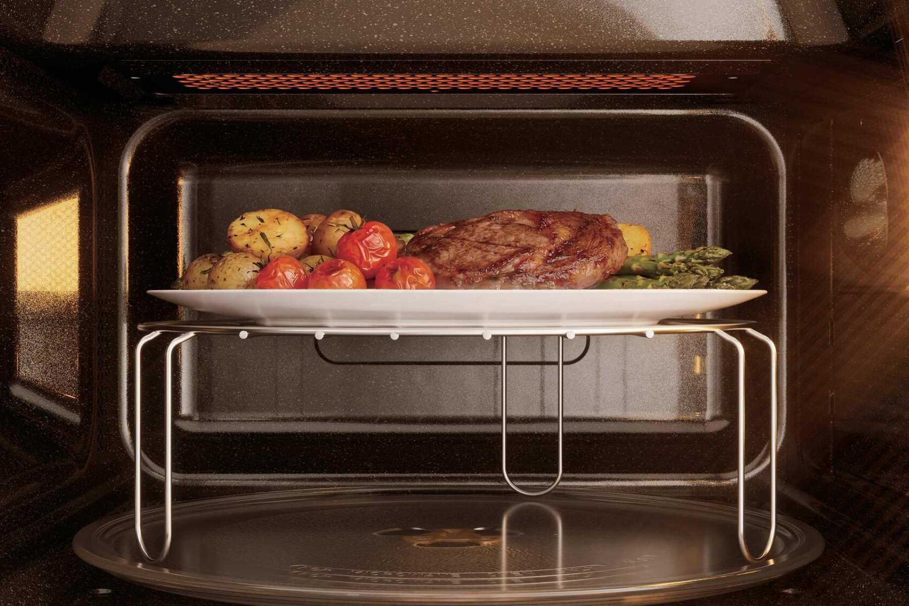 Un plato con bistec, patatas, tomates y espárragos sobre una rejilla dentro de un horno.