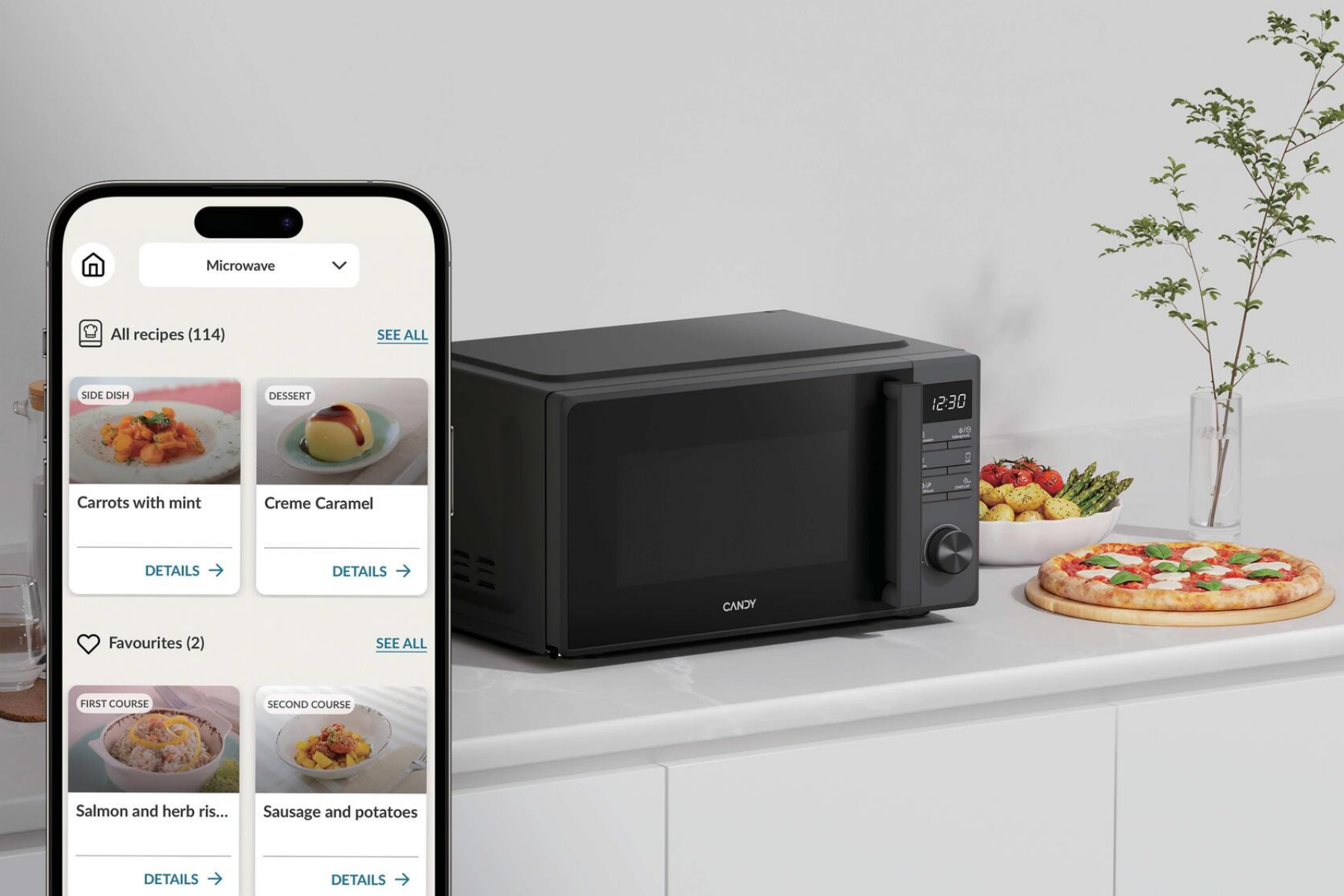 Un teléfono muestra una app de recetas, junto a un microondas negro, pizza y comida en una encimera.