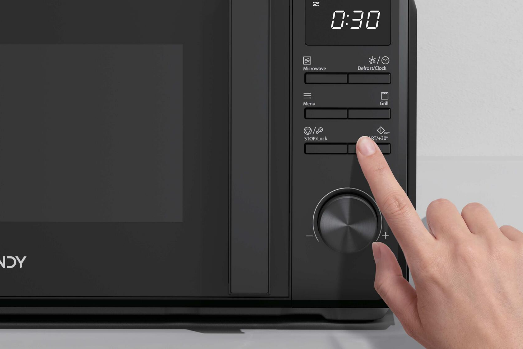 Una mano presiona los botones y gira la perilla en el panel de control digital de un microondas negro.