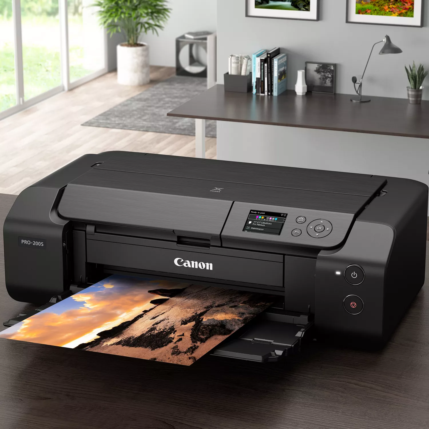 Czarna drukarka Canon PRO-200S stoi na drewnianym biurku, drukując zdjęcie plaży.