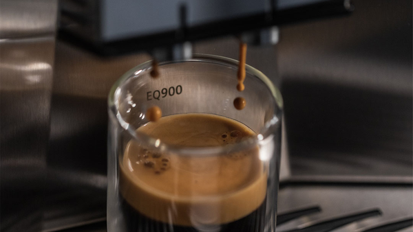 EQ900 yazılı cam bir bardağa kahve makinesinden akan taze espresso.