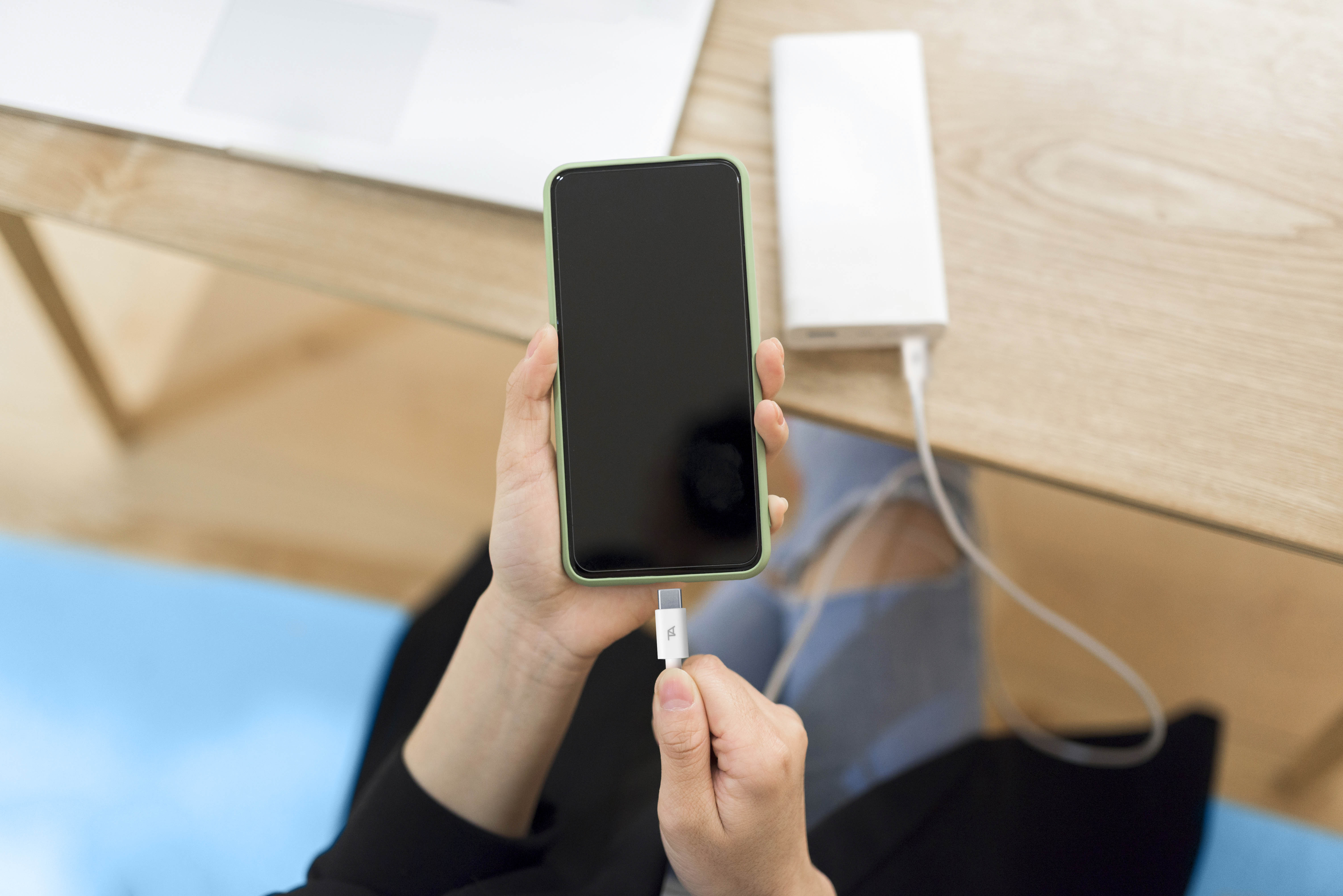 Eine Person verbindet ein Ladekabel mit einer Powerbank und einem Smartphone am Holztisch.