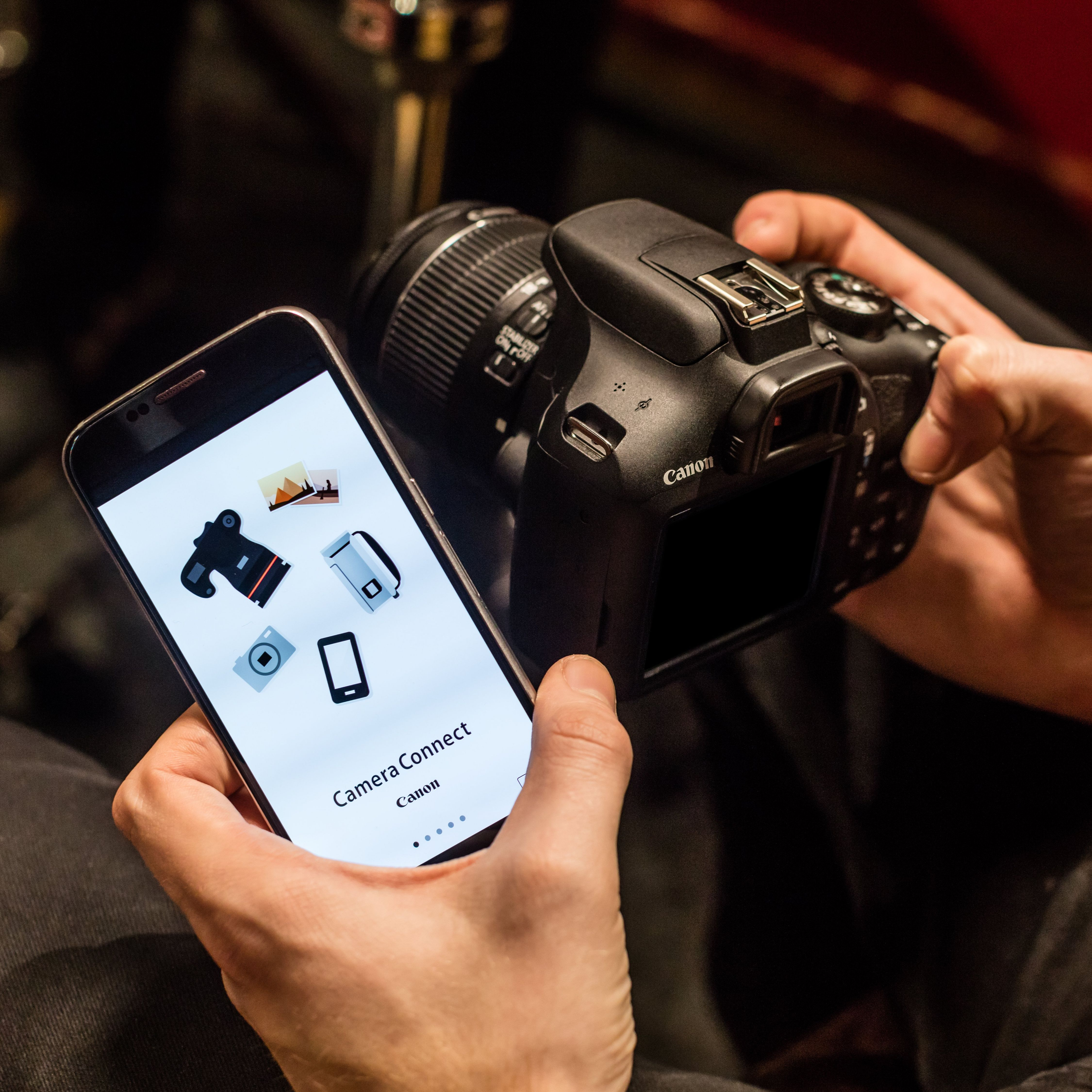 Quelqu'un tient un smartphone affichant l'application Canon Camera Connect près d'un appareil reflex.