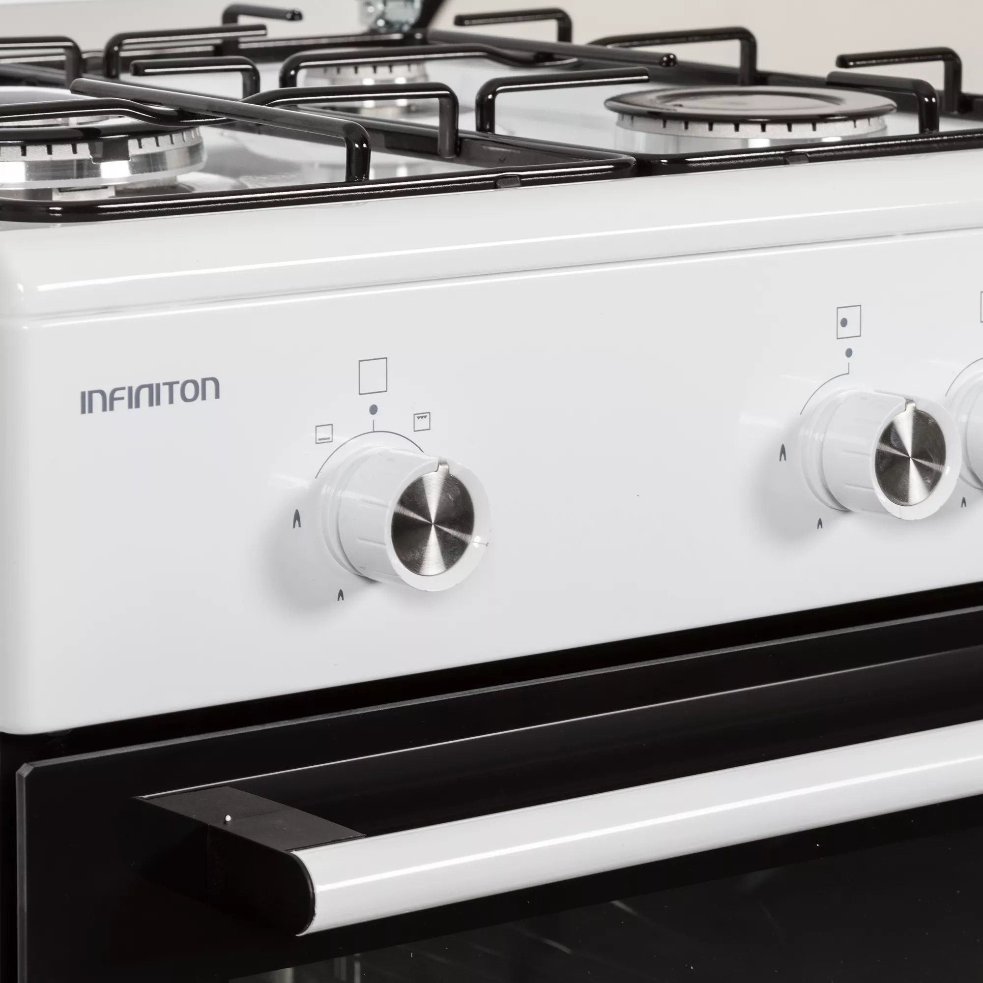 Primer plano de una cocina de gas blanca Infiniton con mandos, quemadores y tirador de horno.