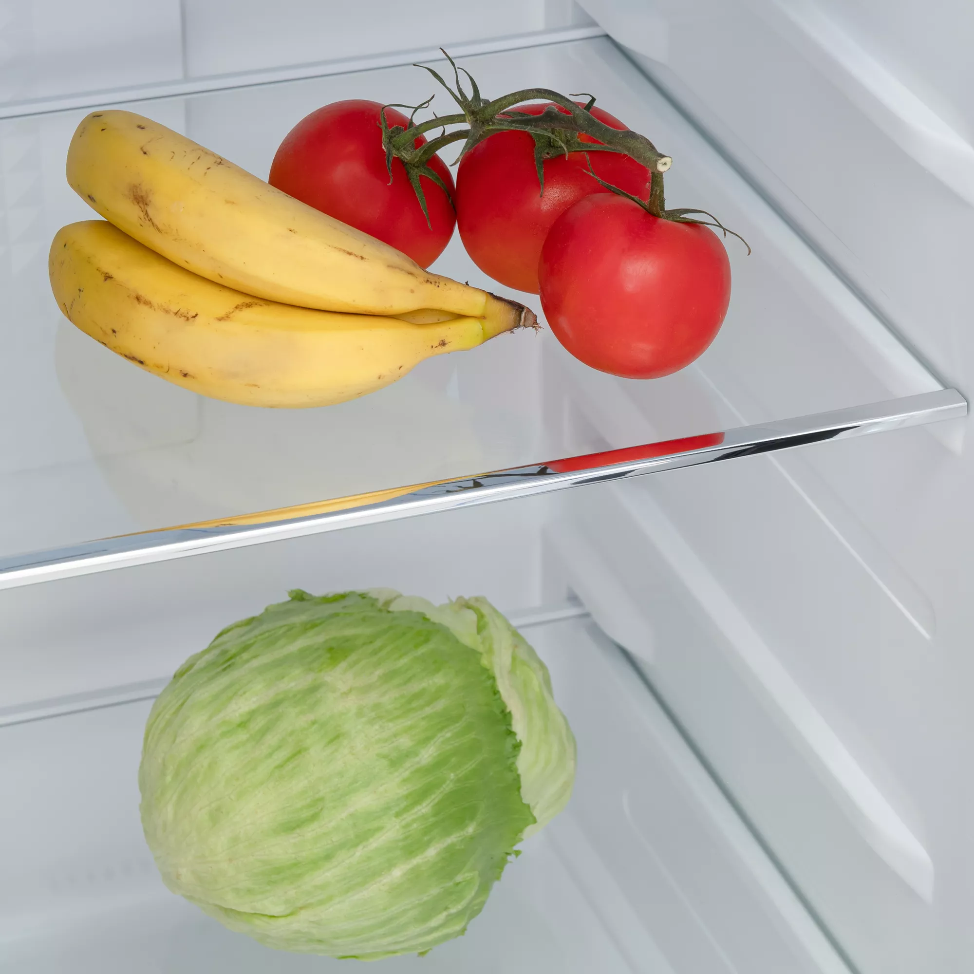 Dos plátanos y tres tomates en el estante superior de la nevera, y una lechuga abajo.