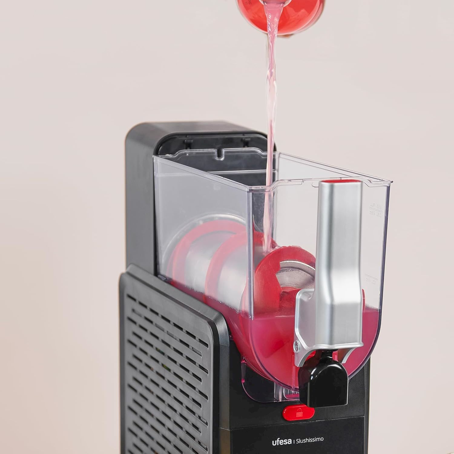 Del liquido rosso viene versato da un contenitore nella camera trasparente di una macchina Ufesa Slushissimo nera.
