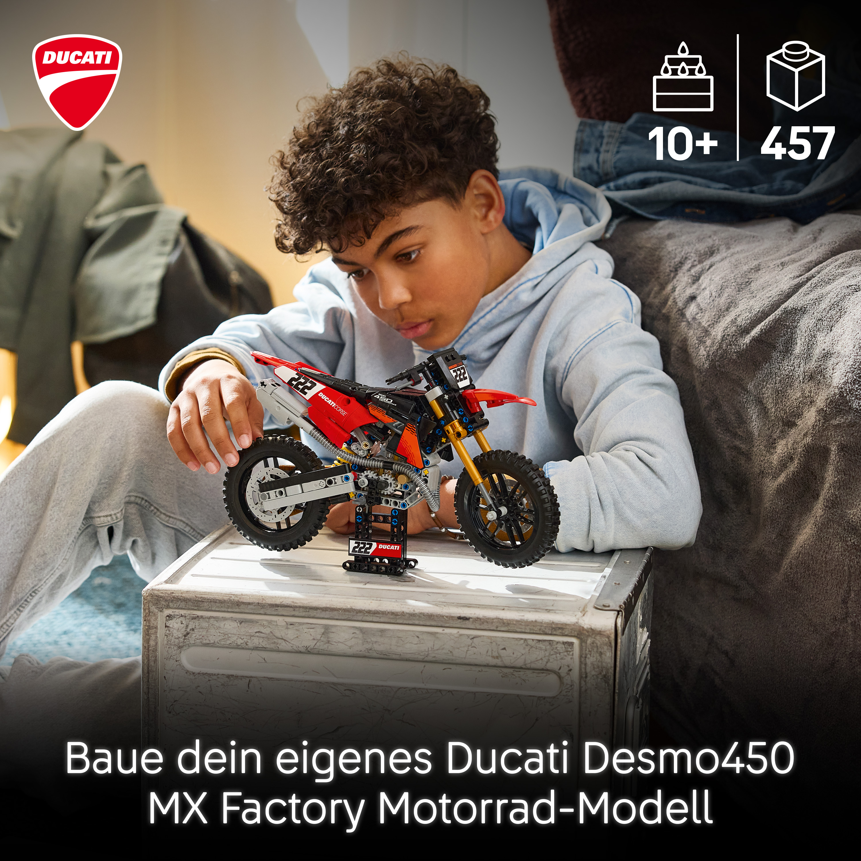Ein Junge baut ein rot-schwarzes Lego Ducati Motorradmodell auf einer weißen Kiste.