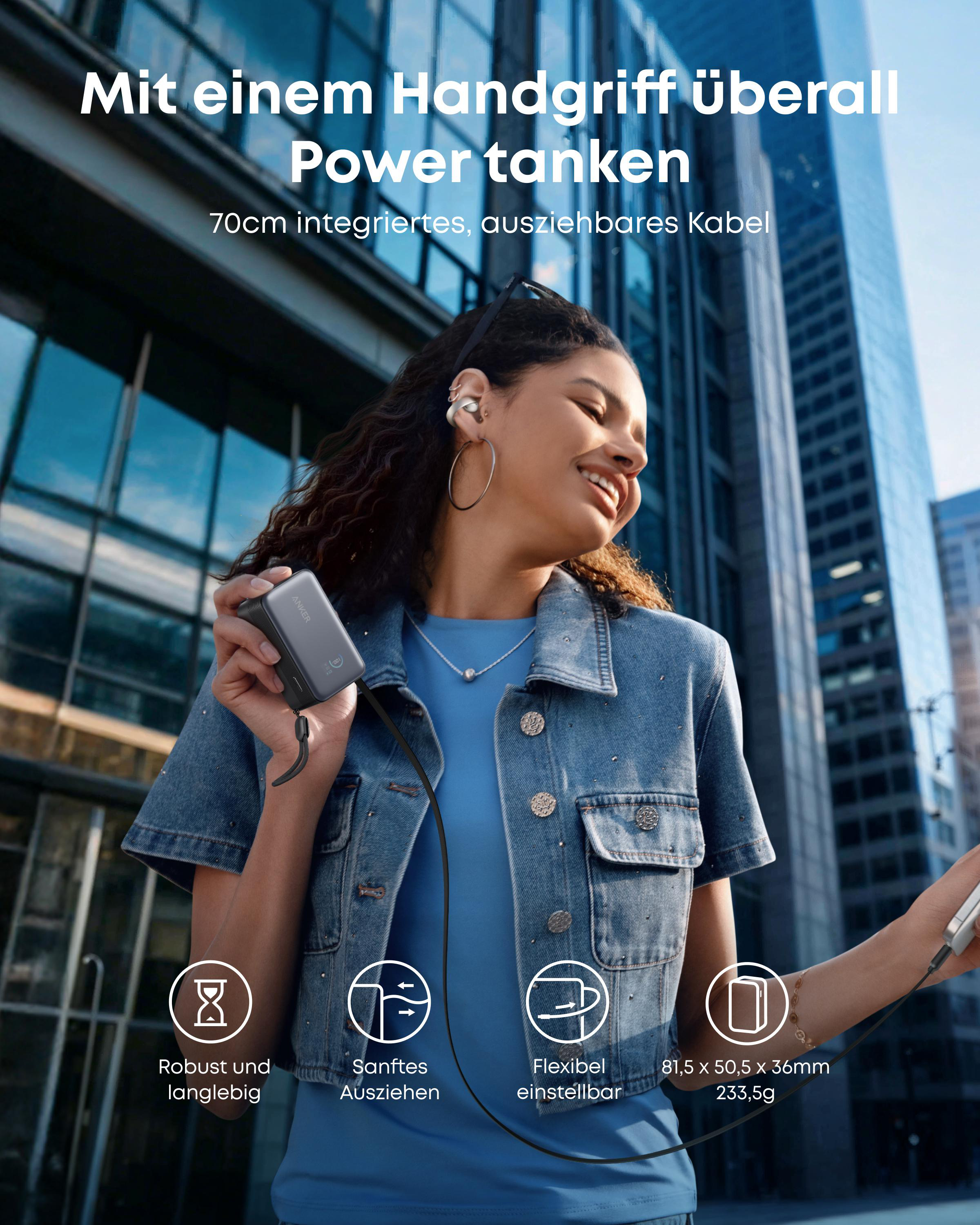 Eine Frau in einer Stadt hält eine kleine Anker Powerbank mit integriertem Kabel in der Hand.