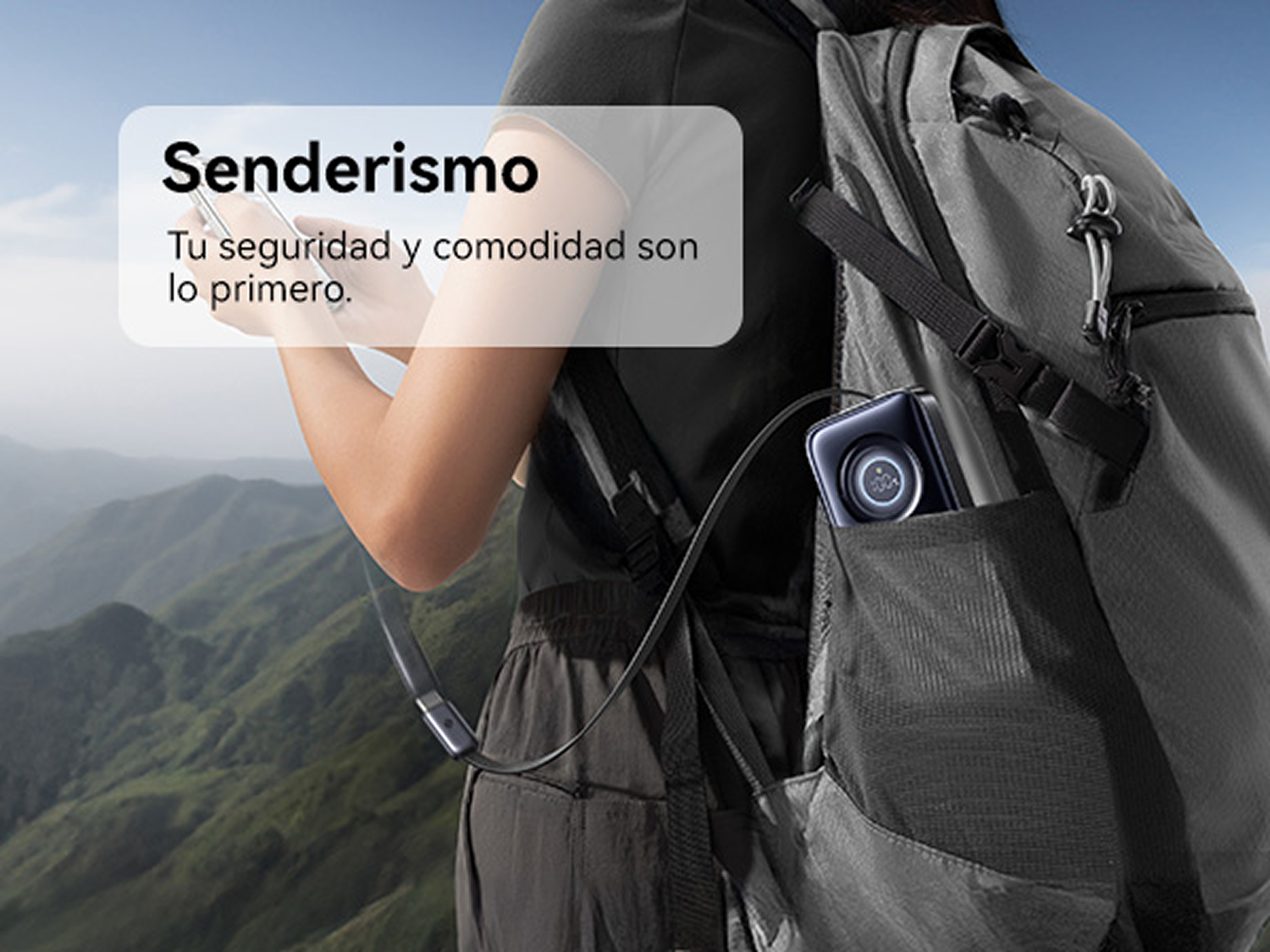 Senderista con mochila gris y batería externa, con montañas verdes de fondo.
