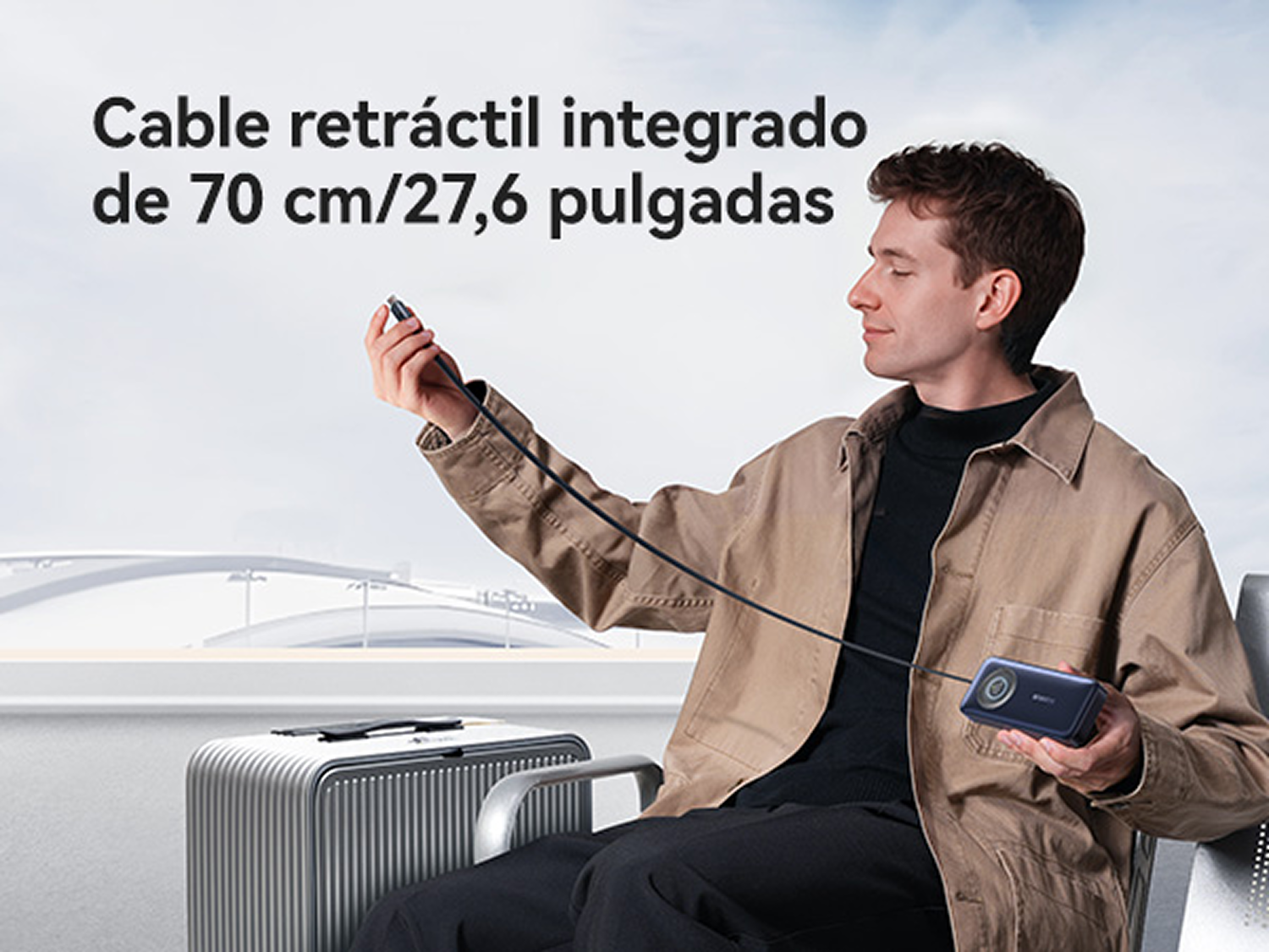 Un hombre con chaqueta beige sostiene una batería externa con cable retráctil largo, junto a una maleta.
