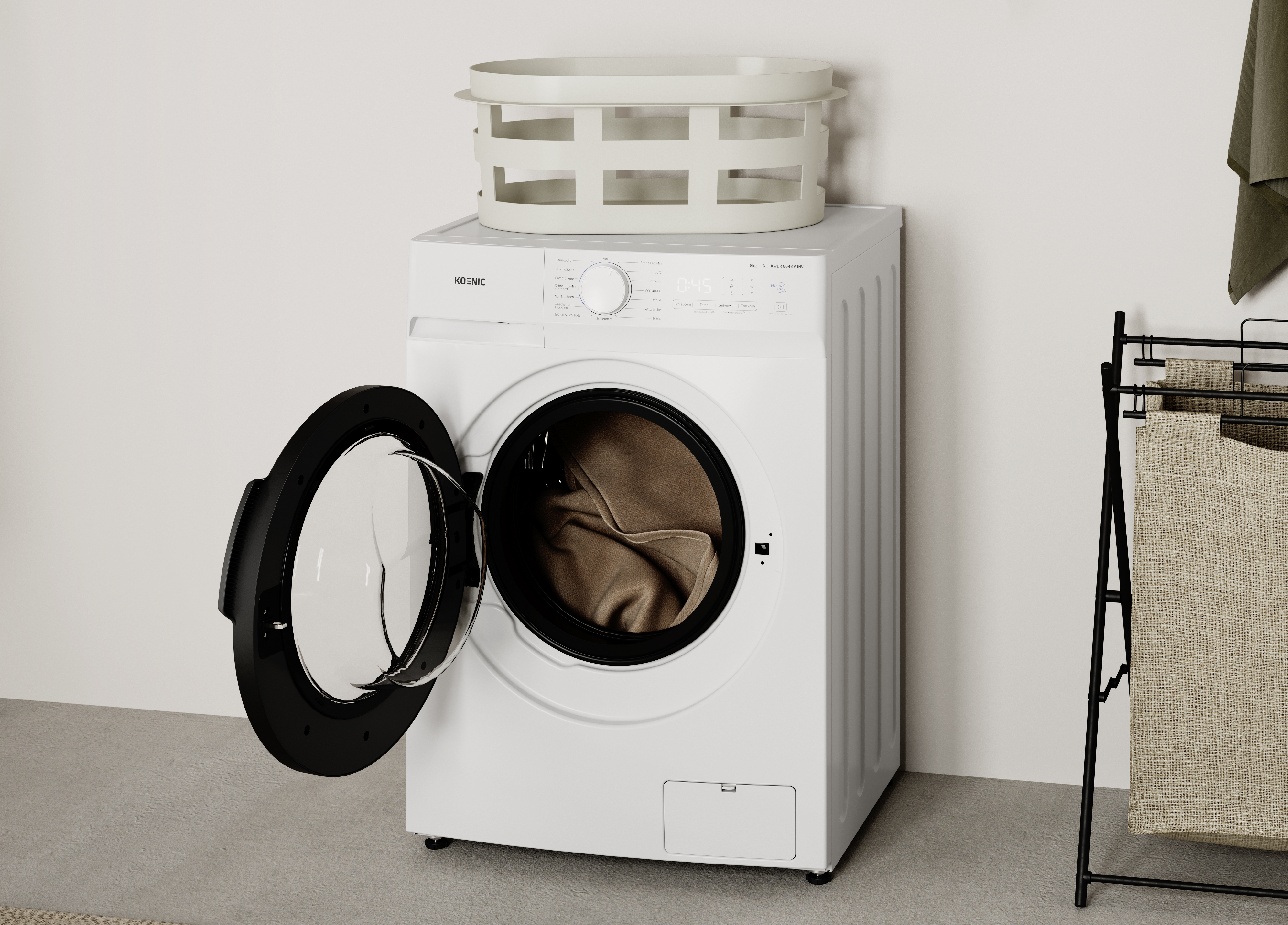Una lavadora blanca con la puerta abierta está en el suelo, con un cesto de ropa encima.