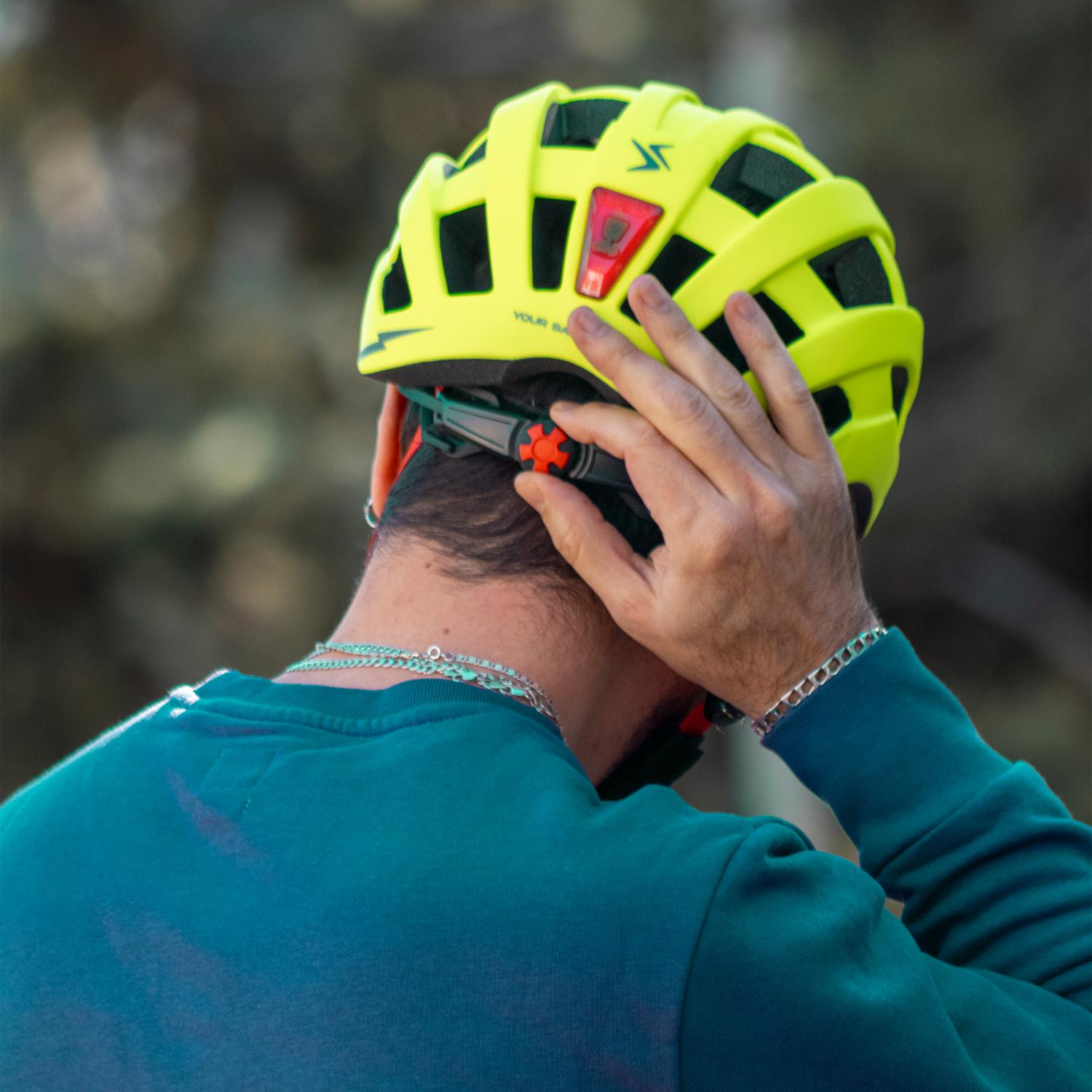Una persona con suéter verde se pone un casco de bicicleta amarillo brillante.