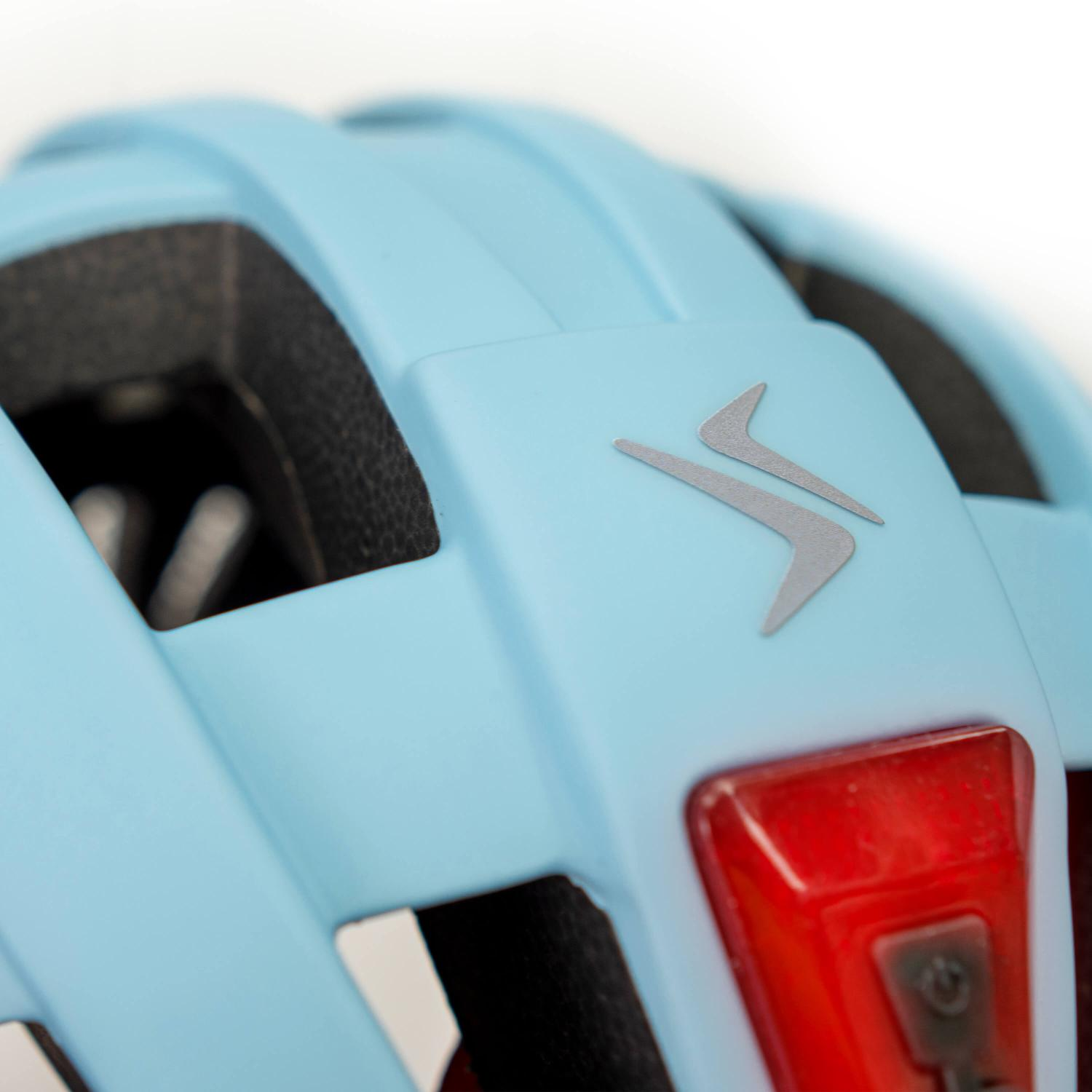 Primer plano de un casco de bicicleta azul claro con un logotipo plateado y una luz trasera roja.