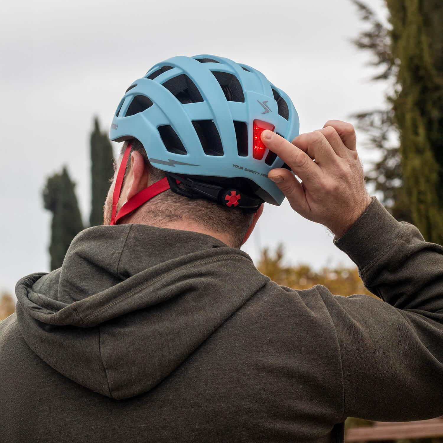 Un hombre con sudadera verde oliva enciende la luz trasera roja de su casco azul claro.