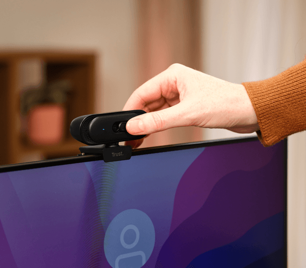 Una mano ajusta una pequeña cámara web negra montada en la parte superior de un monitor.