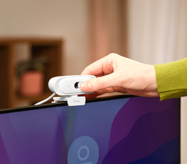 Una mano desliza el obturador de privacidad en una cámara web blanca montada en un monitor.