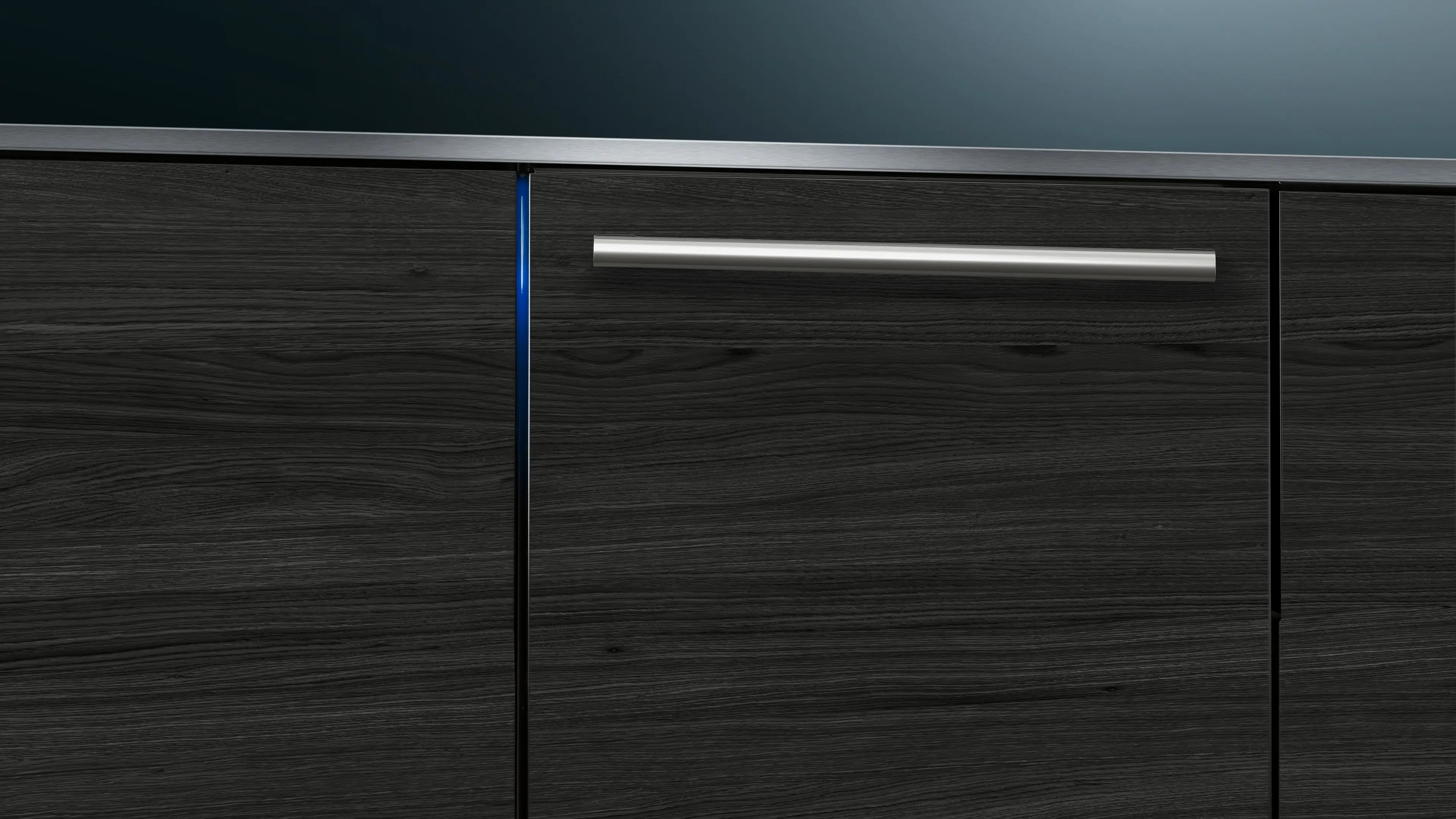 Gabinetes de madera oscura con tirador plateado y luz de acento azul bajo una encimera de acero inoxidable.