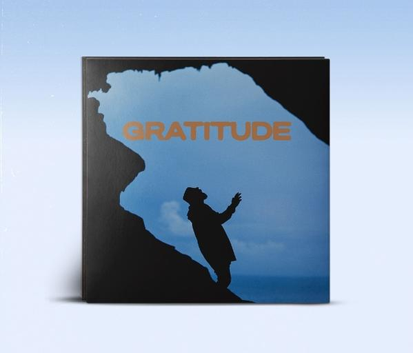 Ein Buchumschlag mit dem Wort GRATITUDE, der Silhouette einer Person in einer Höhle und blauem Himmel.