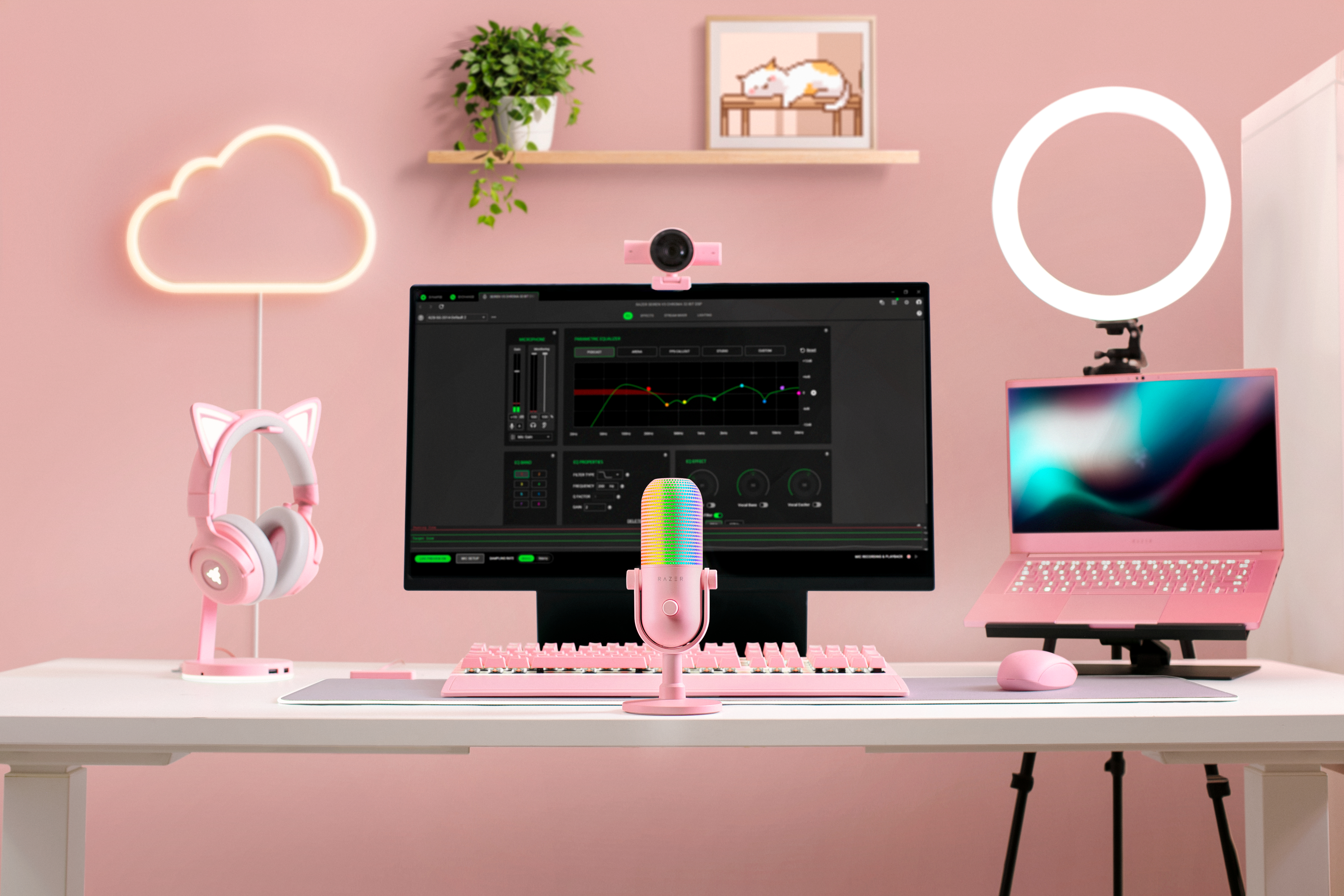 Ein rosafarbenes Streaming-Setup mit Monitor, Mikrofon, Laptop und Ringlicht vor einer rosa Wand.
