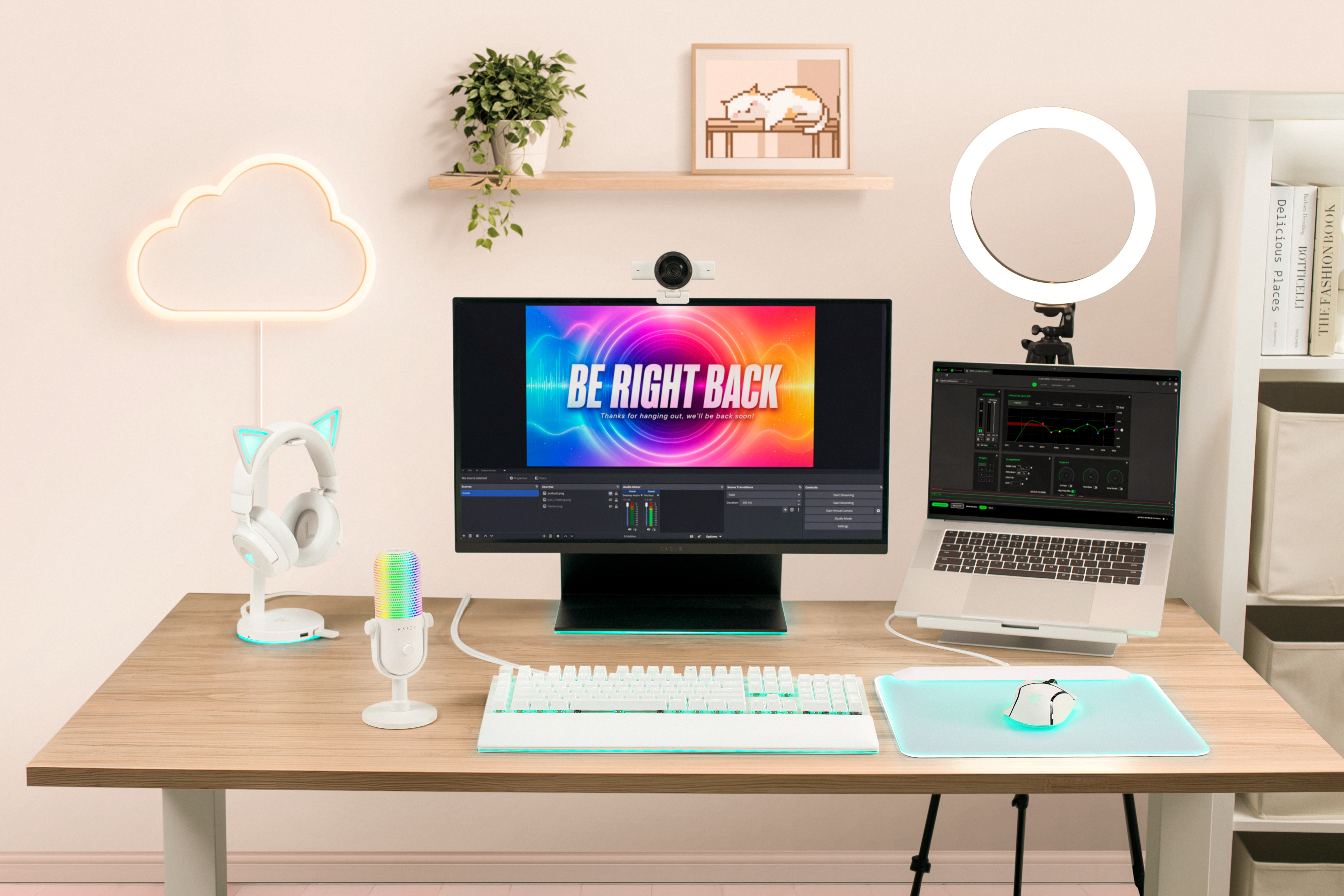 Ein aufgeräumtes Streaming-Setup mit Monitor, Laptop, Regenbogen-Mikrofon, weißer Tastatur, Mauspad und Neon-Wolke.