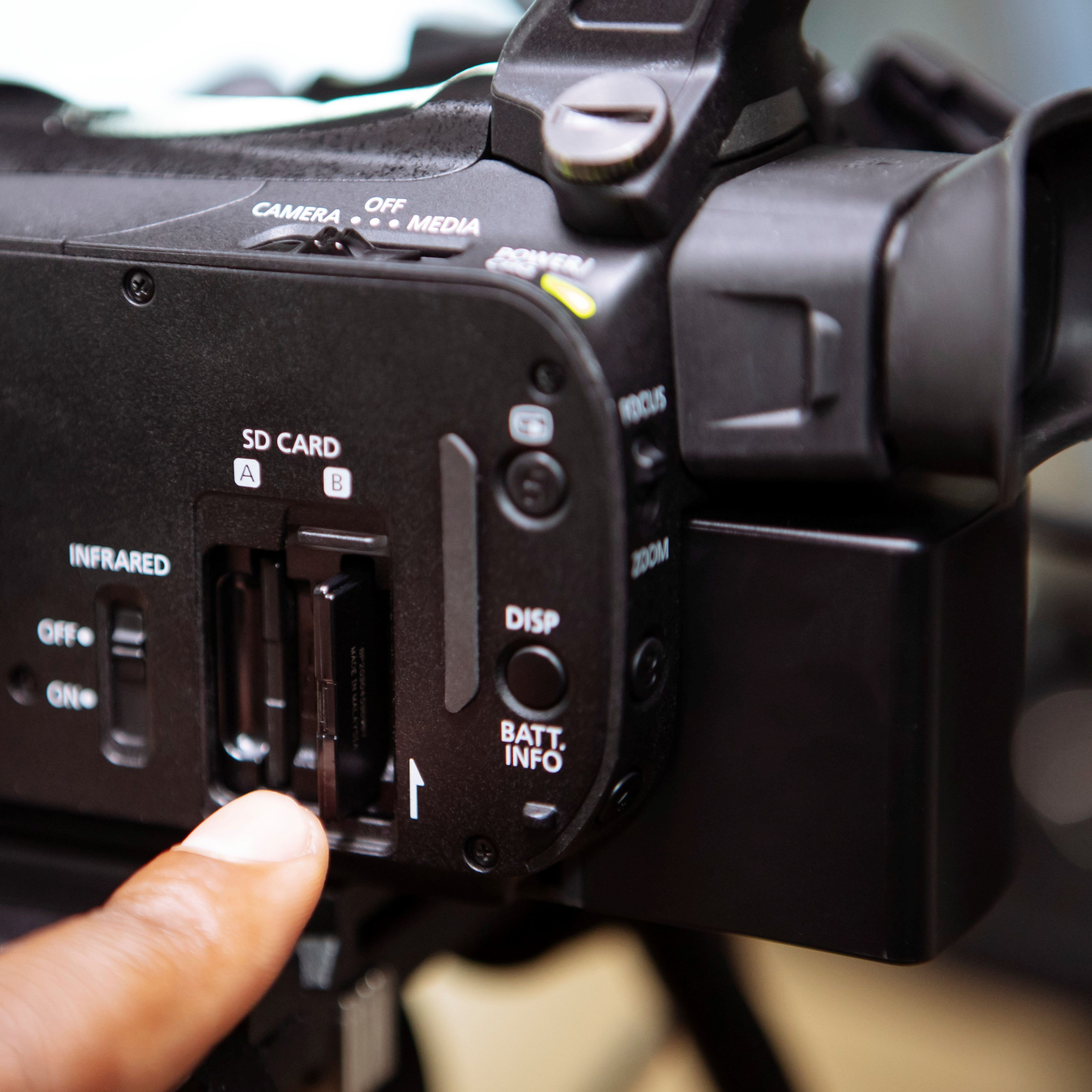 Un doigt insère une carte SD dans la fente d'une caméra vidéo noire.