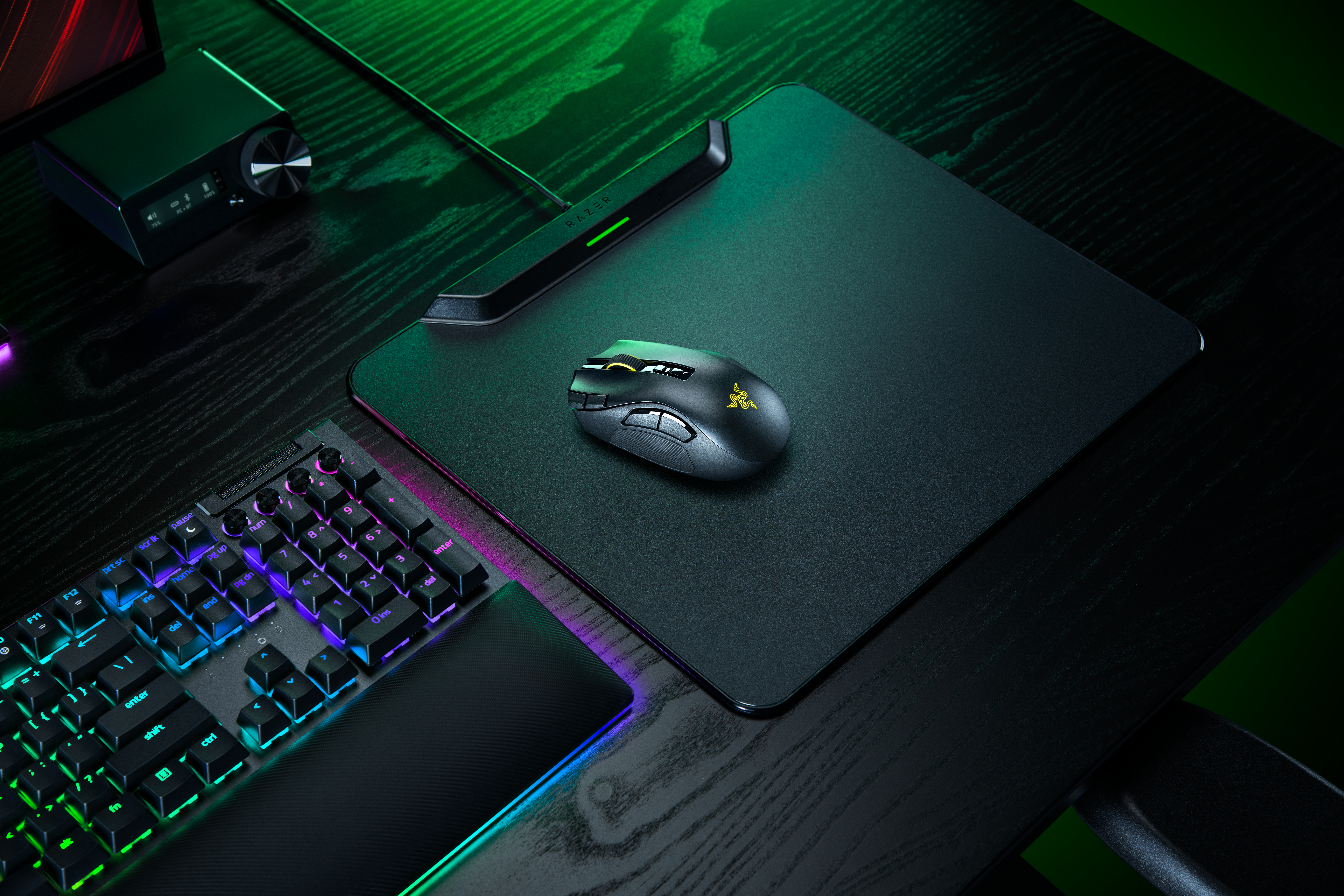 Eine schwarze Gaming-Maus auf einem Mauspad, daneben eine beleuchtete Tastatur auf einem Holztisch.