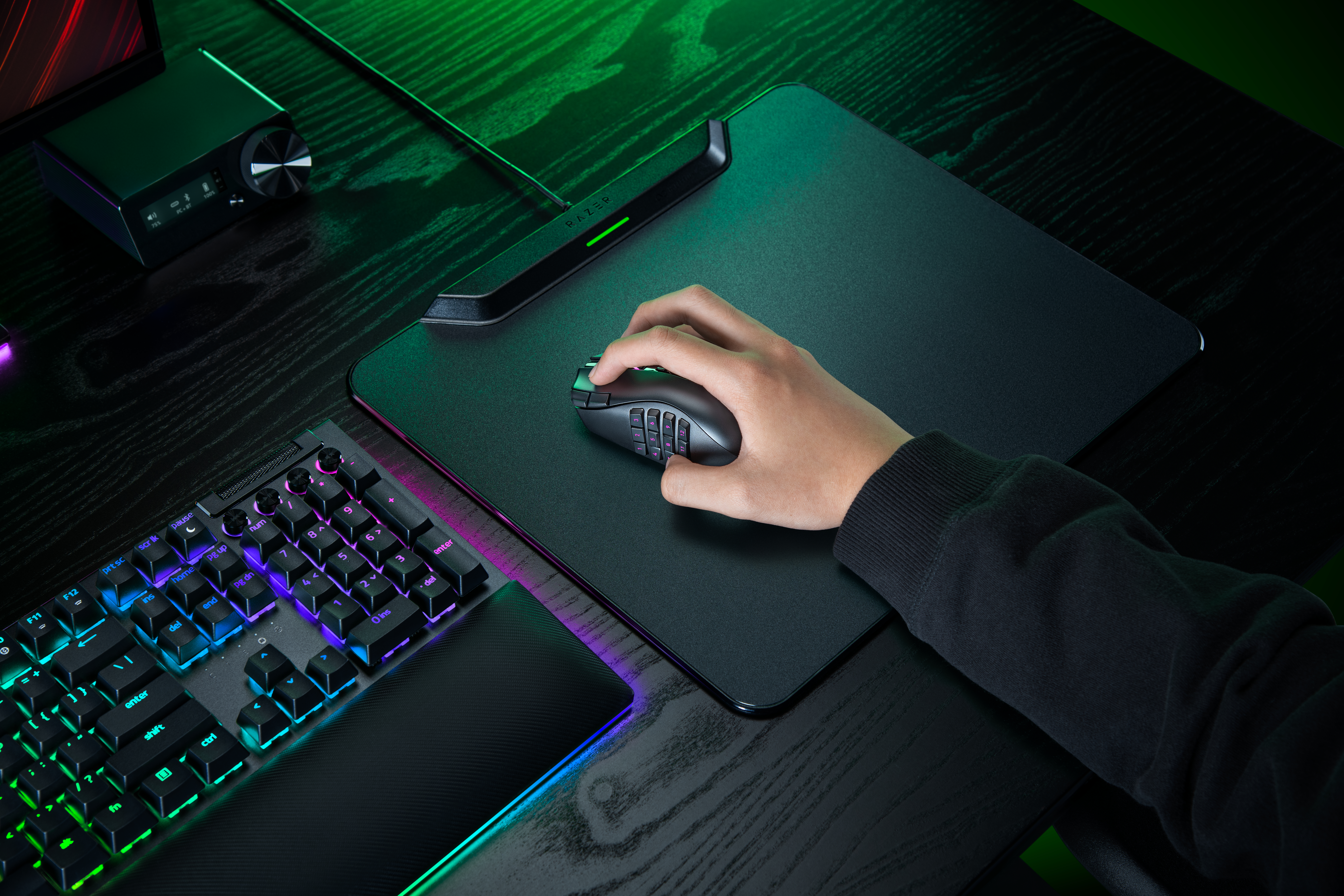 Eine Hand benutzt eine Gaming-Maus auf einem großen Mauspad, mit einer hell beleuchteten RGB-Tastatur auf einem Schreibtisch.