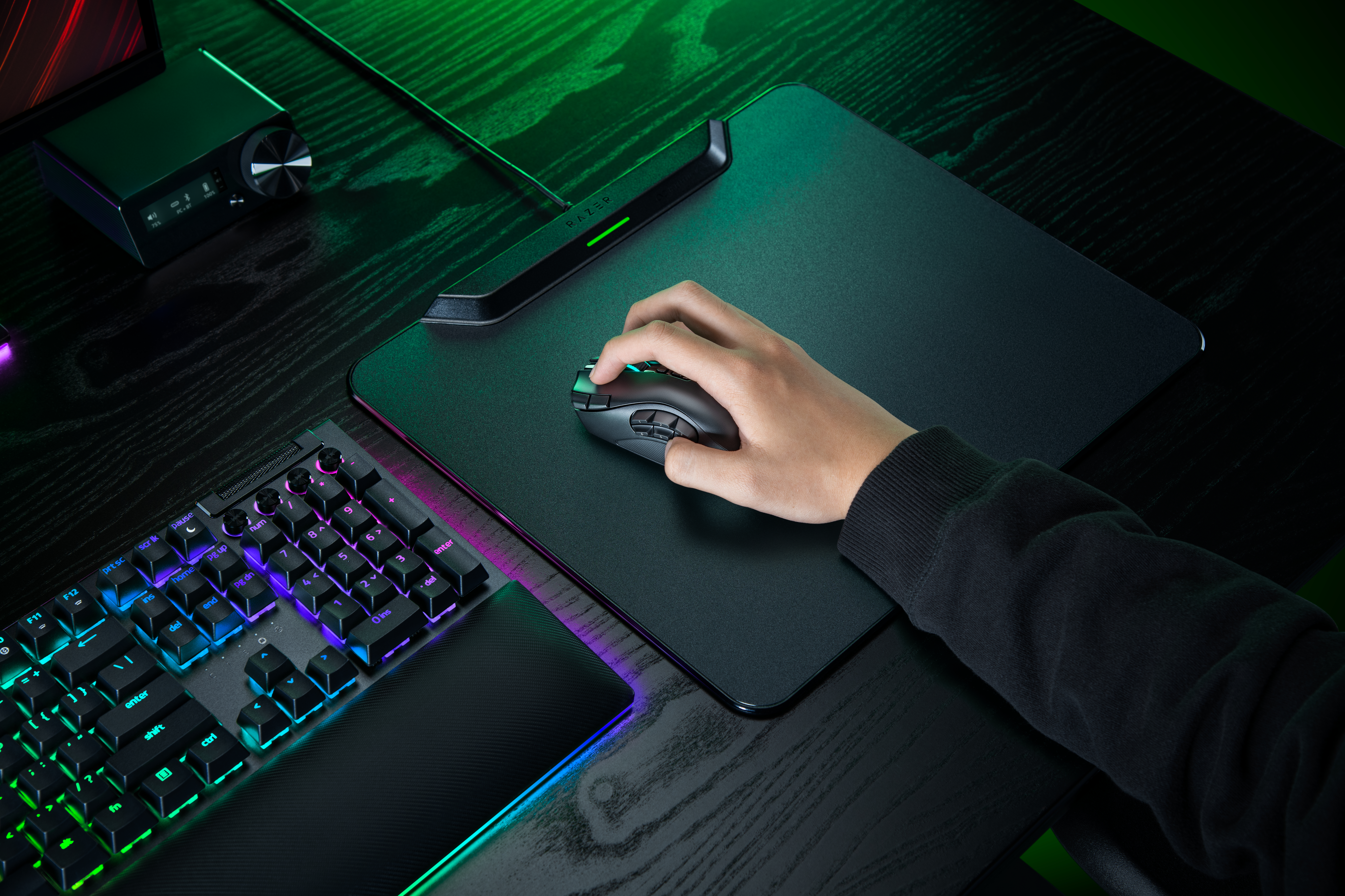 Hand bedient eine schwarze Razer-Maus auf einem Mauspad neben einer beleuchteten Tastatur.