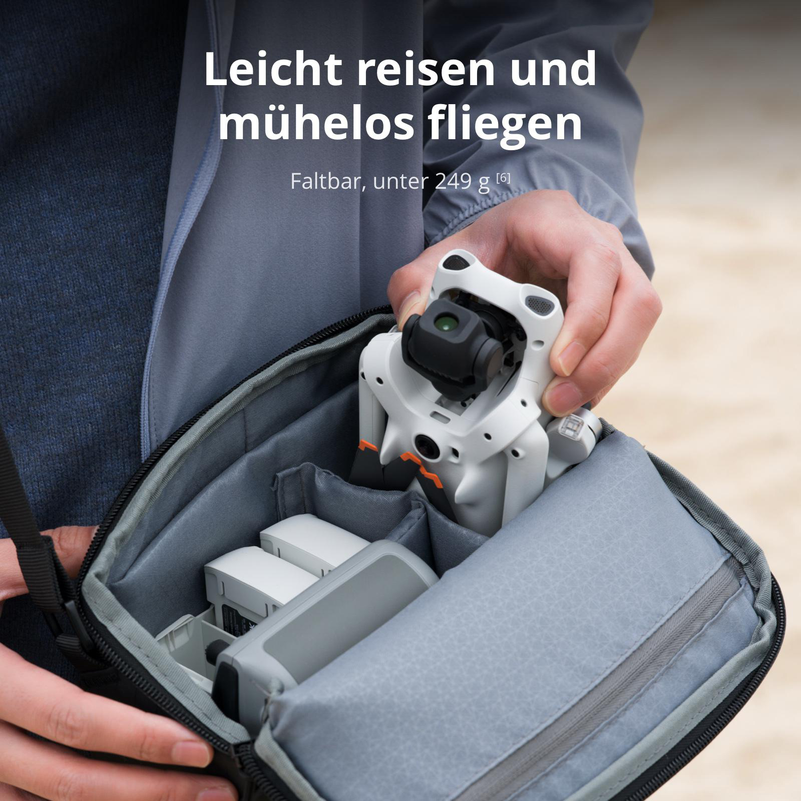 Eine Person packt eine kompakte weiße Drohne und Zubehör in eine graue Umhängetasche.