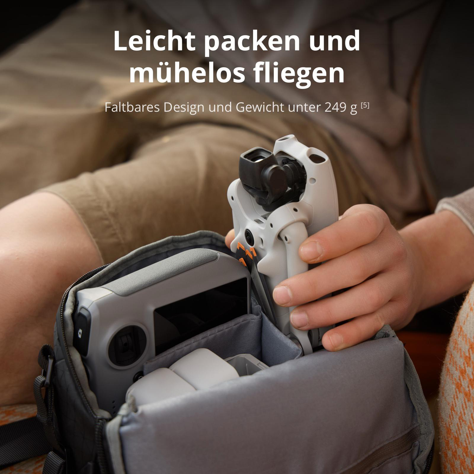 Eine Hand nimmt eine faltbare Drohne aus einer offenen, grauen Tasche, in der auch eine Fernbedienung liegt.